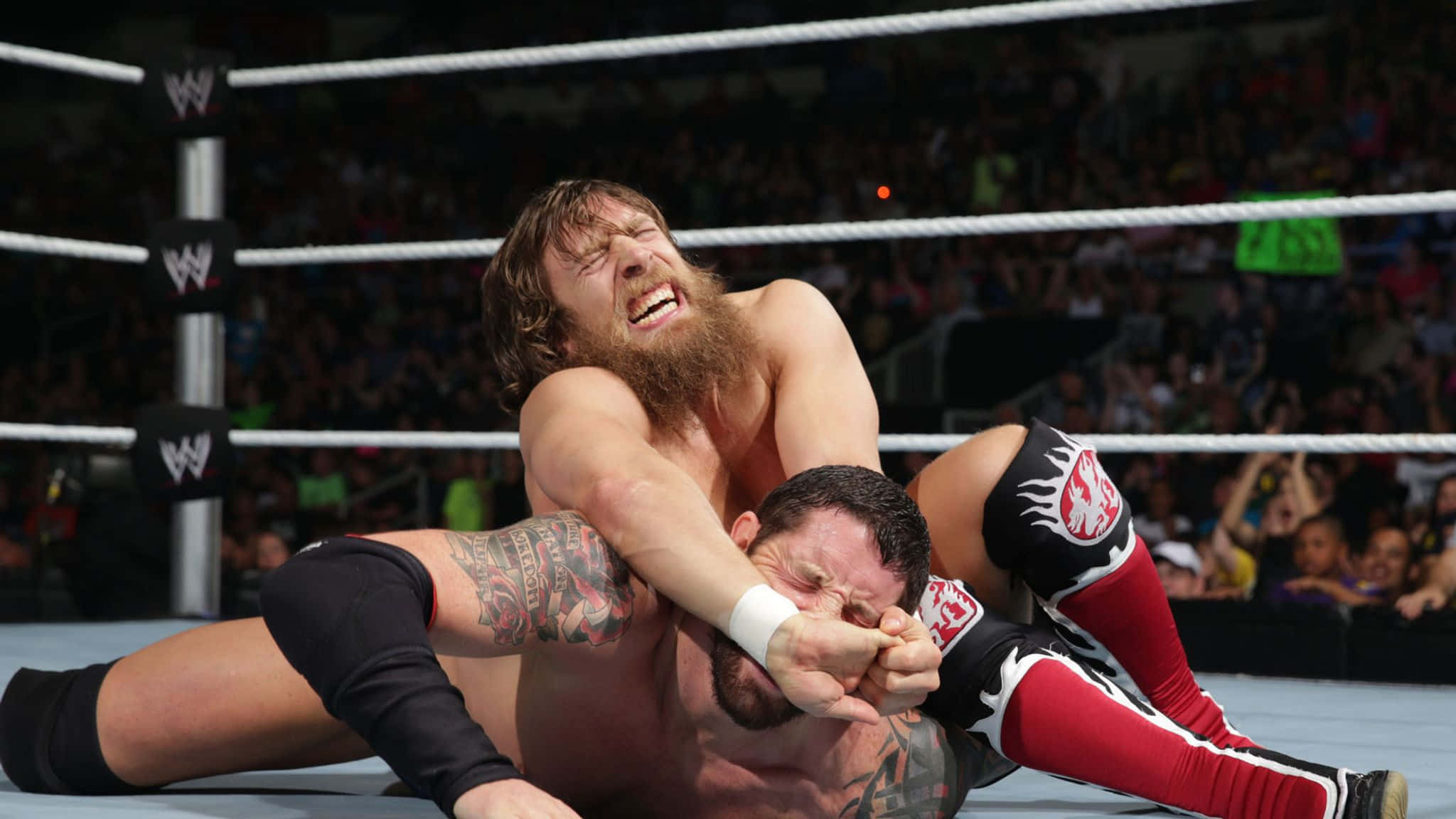 WWE 桌布 壁紙 — 兩名摔角手在擂台上激烈纏鬥，背景是咆哮的人群。