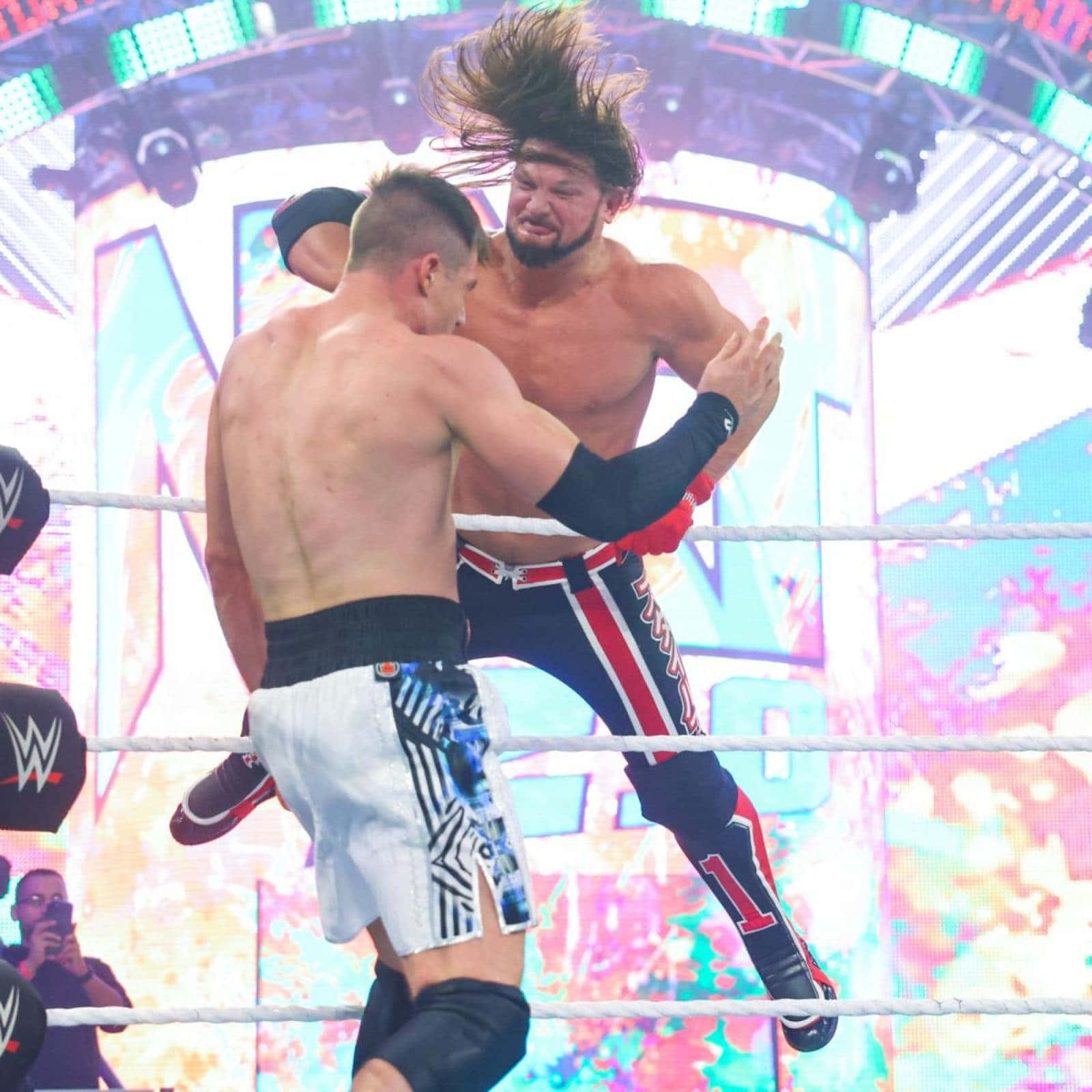 WWE 桌布 壁紙 — 兩名摔角手在擂台上碰撞，其中一人凌空施展招式，背景是充滿活力的數位畫面。
