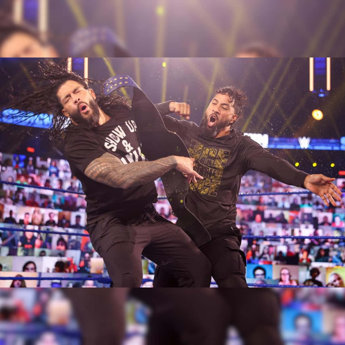 Roman Reigns 桌布 壁紙 — 兩名摔角手在明亮的舞台燈光下於擂台上交鋒，繩索上有一群虛擬粉絲。