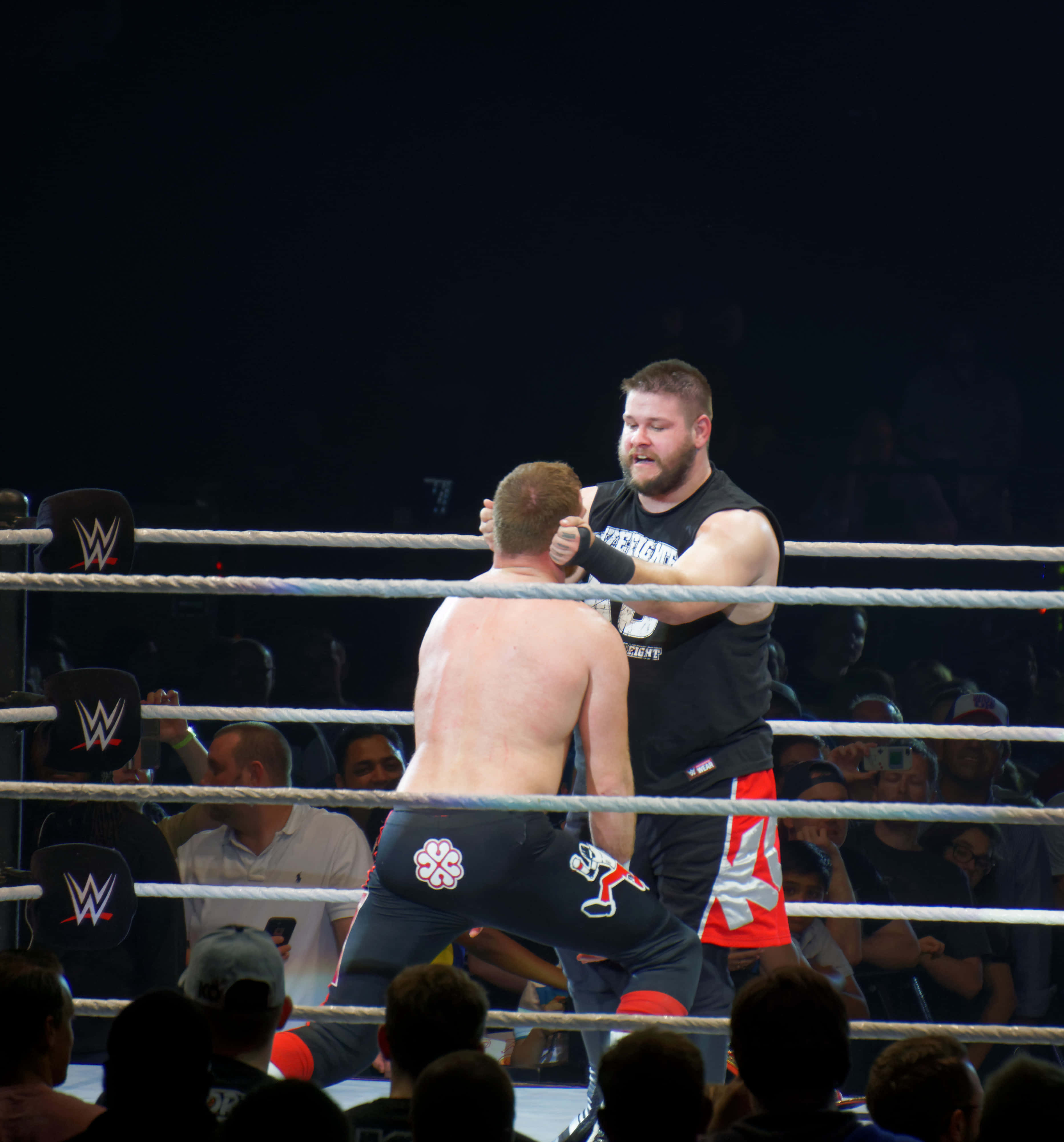 sami zayn 桌布 壁紙 — 兩名摔角手在燈光明亮的擂台上激烈纏鬥，觀眾在場館燈光下觀看。