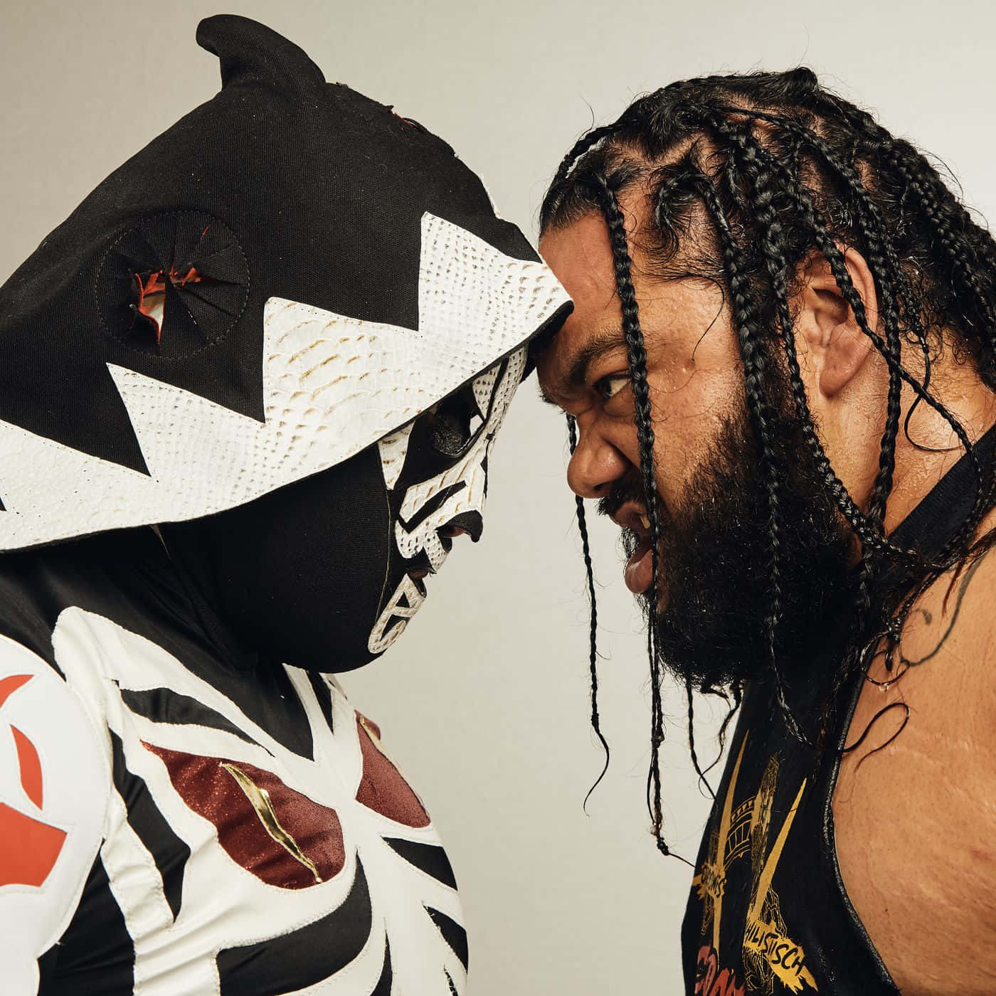 WWE 桌布 壁紙 — 兩名摔角手激烈對峙，一人戴著黑白面具，另一人有辮子頭髮和鬍鬚。