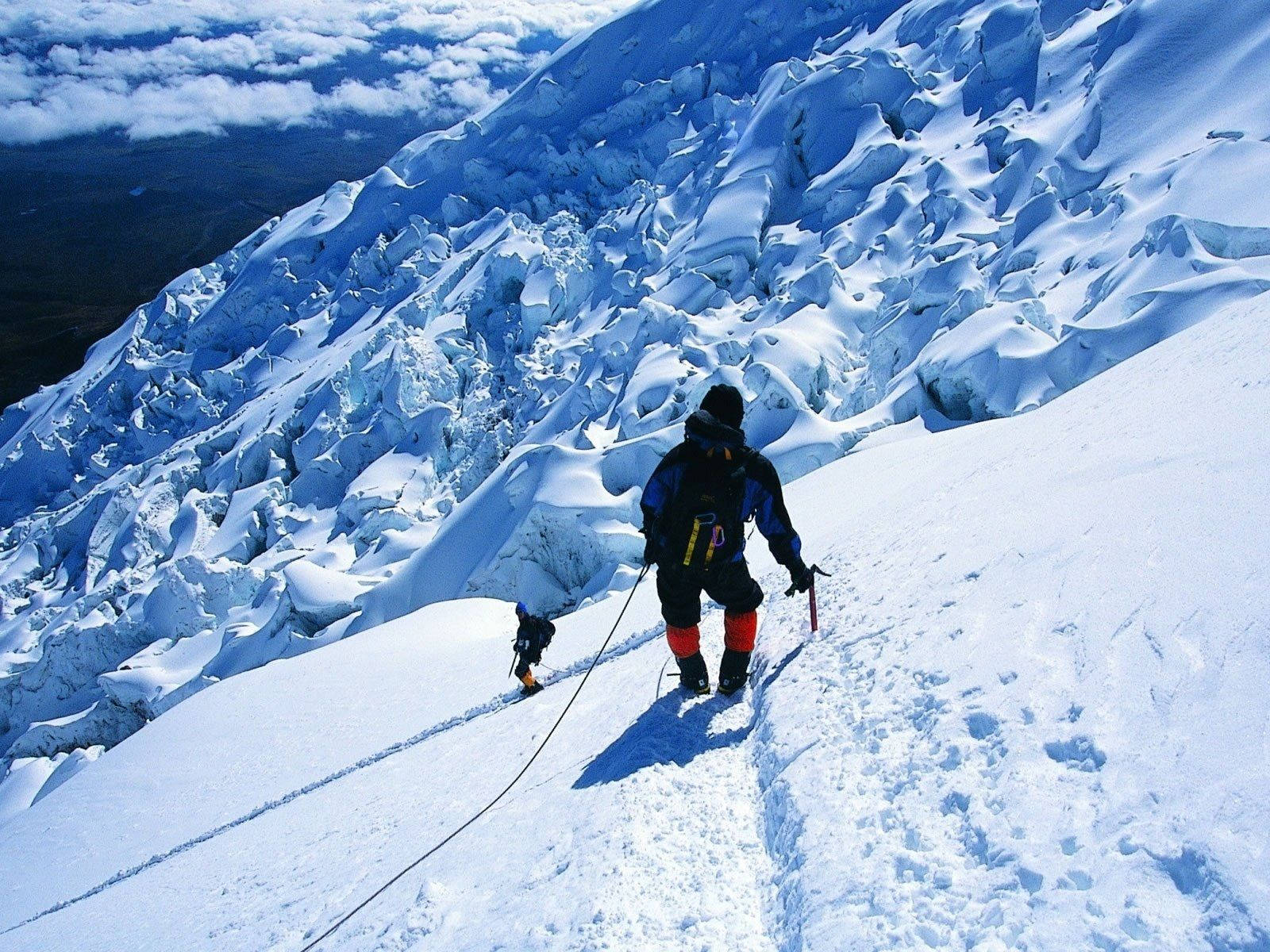 山景 桌布 壁紙 — 兩名攀岩者在明亮的藍天下攀登陡峭的積雪冰川，下方有雲層。