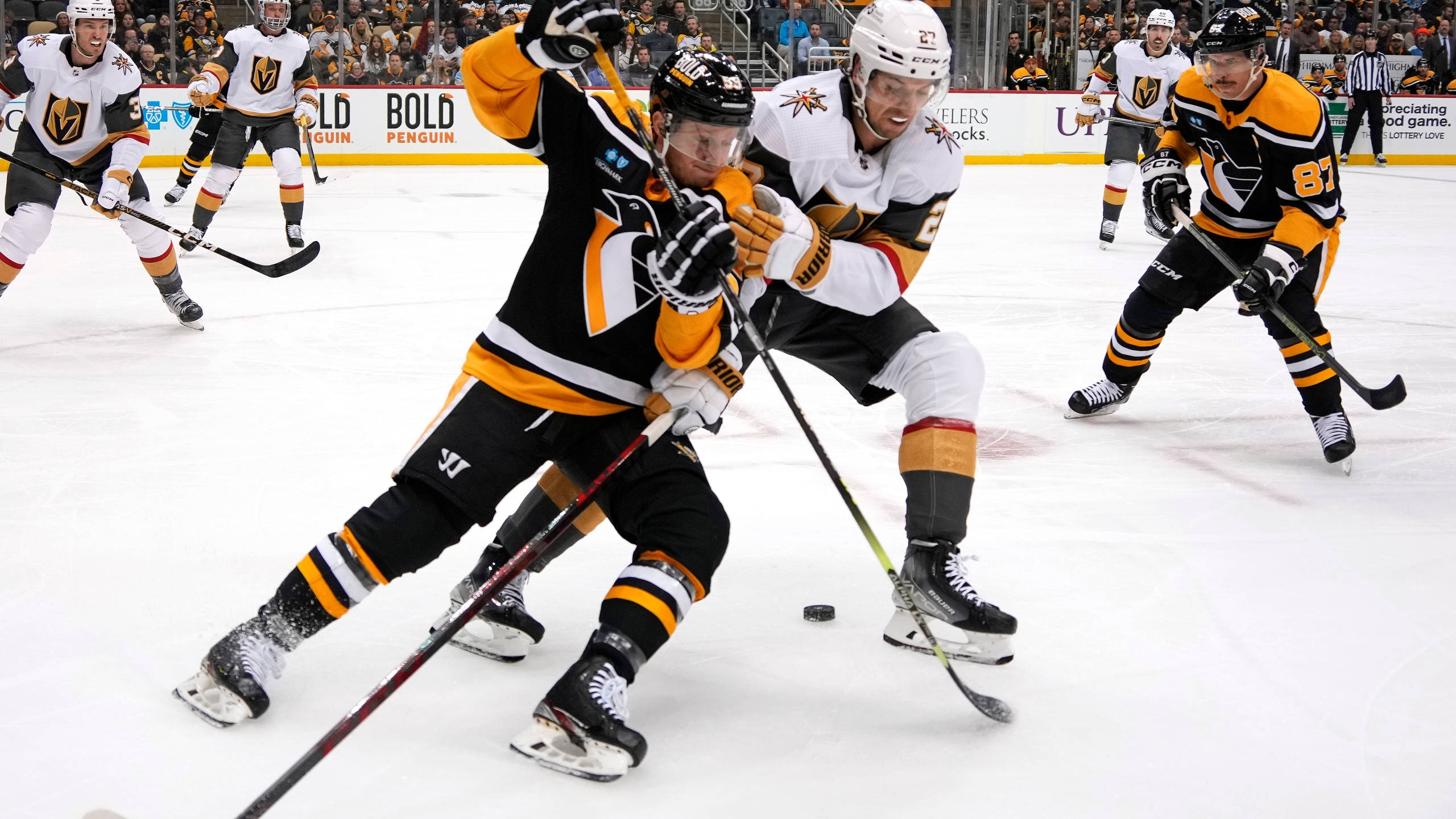 hockey 桌布 壁紙 — 兩名曲棍球運動員在明亮的冰場上激烈爭奪冰球，背景有隊友和觀眾。