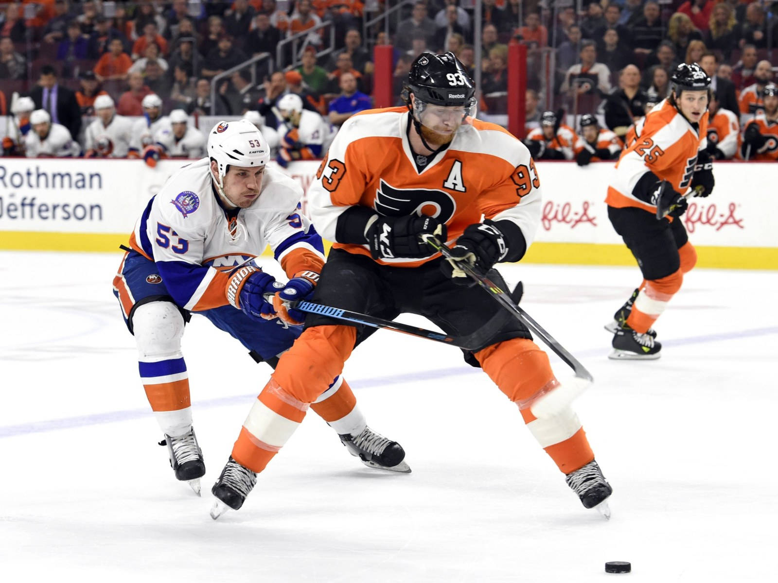 hockey 桌布 壁紙 — 兩名曲棍球運動員在燈光明亮的冰場上激烈爭奪冰球，背景有觀眾。