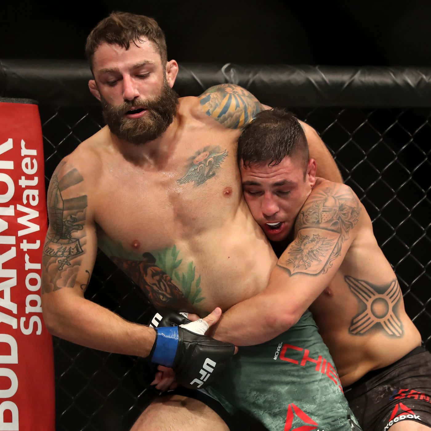 MMA 桌布 壁紙 — 兩名有刺青的MMA拳手在明亮的場館燈光下，於UFC比賽期間在鐵籠內激烈纏鬥。