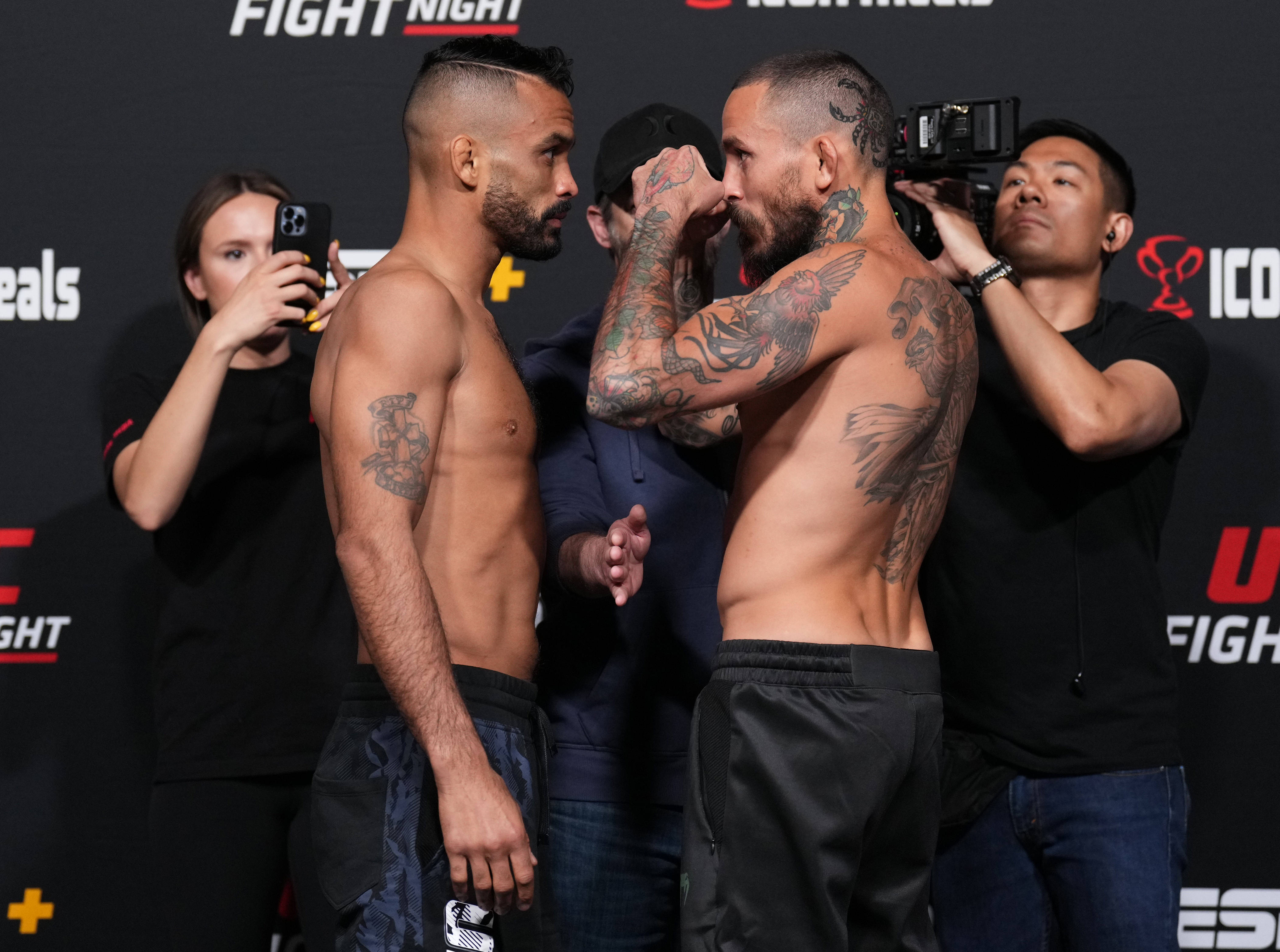 UFC 桌布 壁紙 — 兩名有刺青的MMA拳手在磅重時激烈對峙，周圍閃光燈不斷。