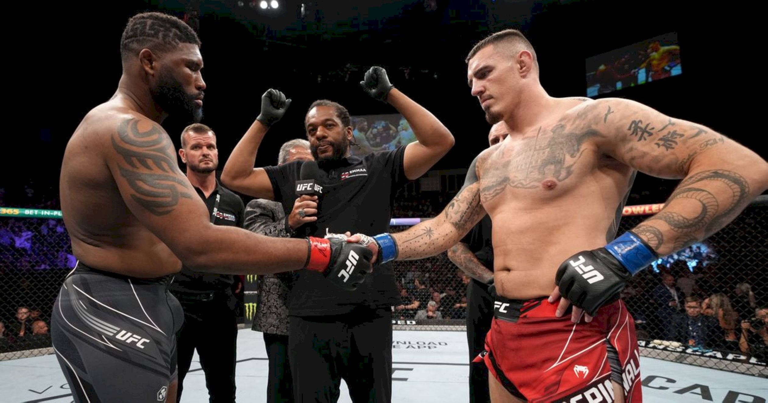 UFC 桌布 壁紙 — 兩名有刺青的UFC拳手在八角籠內，在明亮的場館燈光下，與中間的裁判握手。