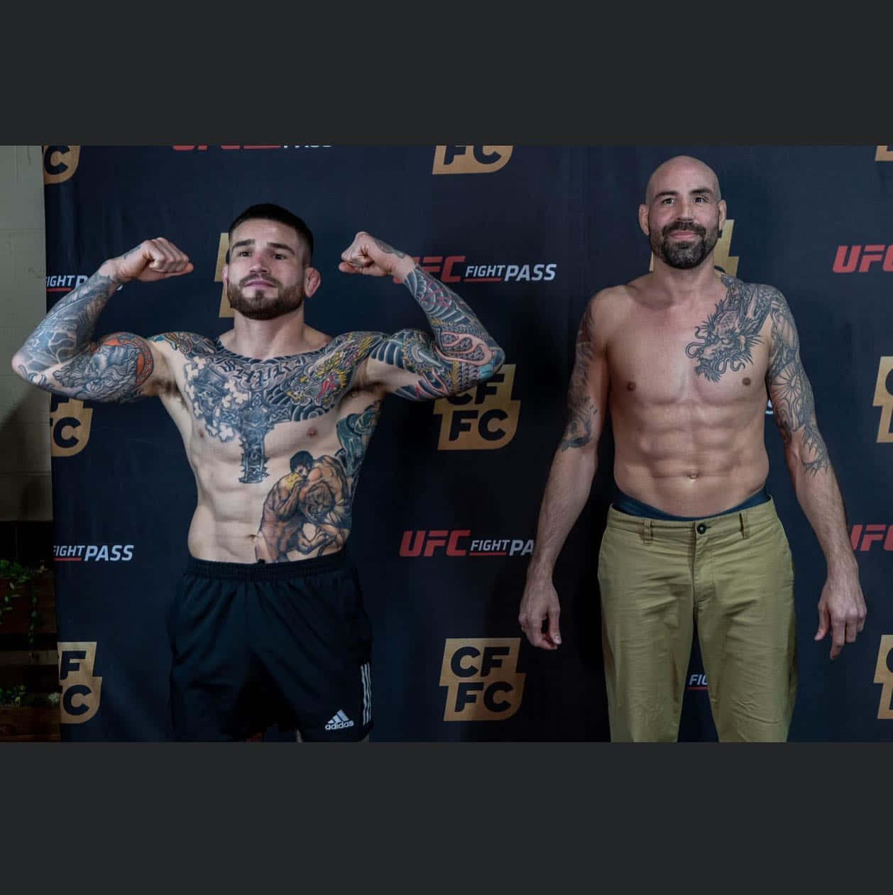 MMA 桌布 壁紙 — 兩名有刺青的UFC拳手在稱重時赤裸上身擺姿勢，一個繃緊肌肉，另一個放鬆地站在有品牌的背景前。