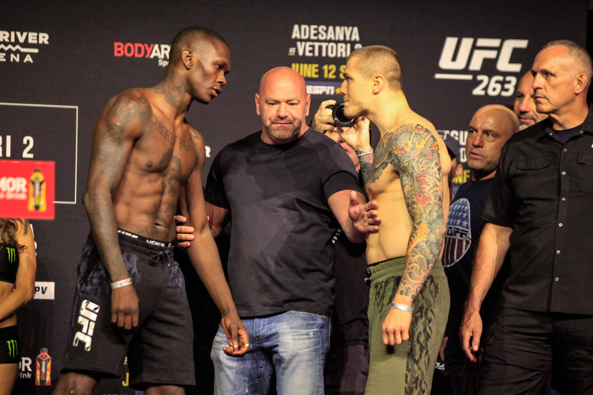 UFC 桌布 壁紙 — 兩名有刺青的UFC拳手在賽前稱重時互相怒視，背景有工作人員和品牌標誌。