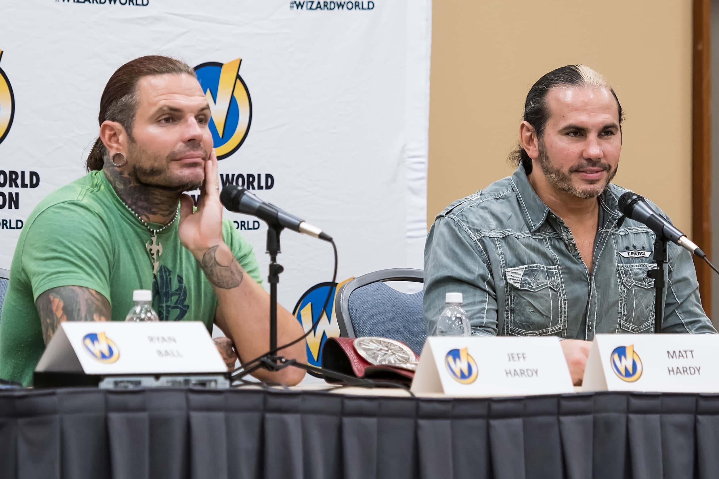 WWE 桌布 壁紙 — 兩名有刺青的摔角手坐在Wizard World會議的座談會桌上，桌上放有麥克風和名牌。