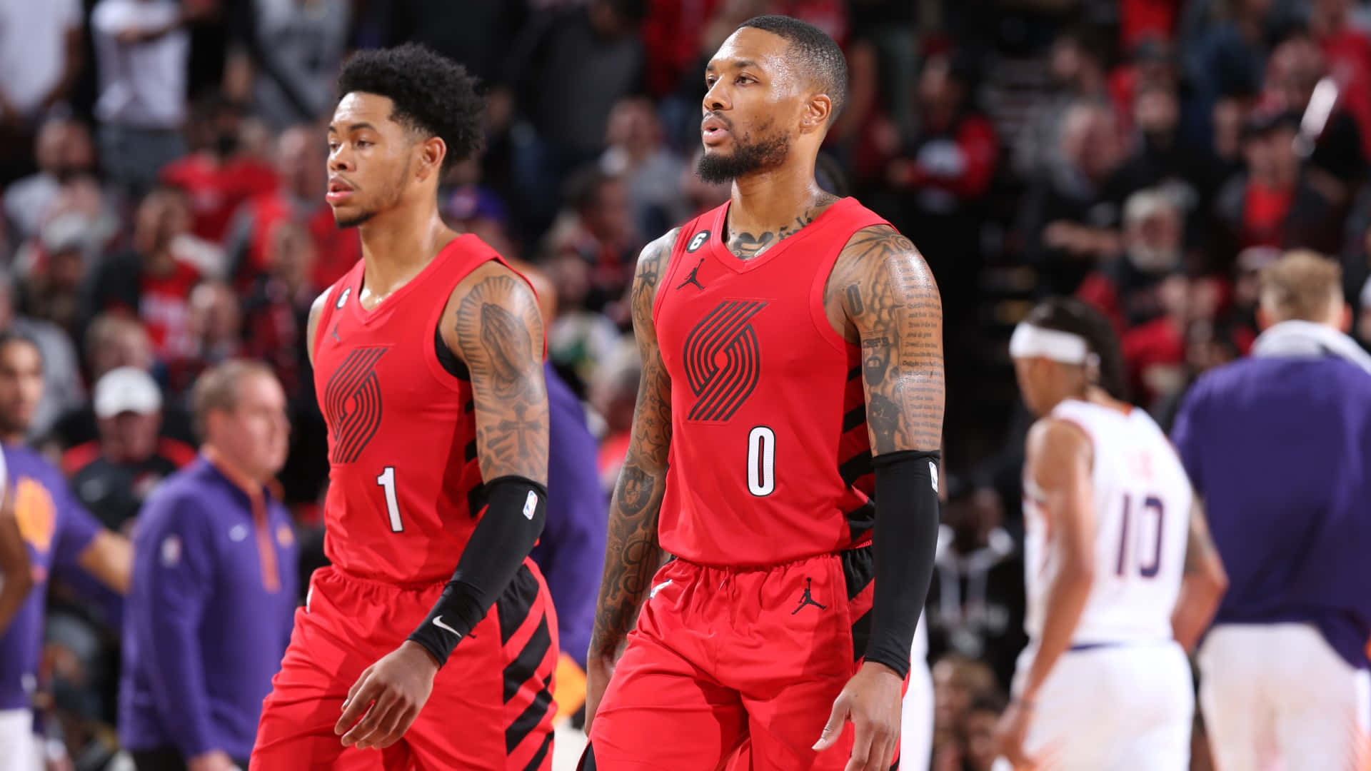 Anfernee Simons 桌布 壁紙 — 兩名有刺青的籃球運動員穿著紅色球衣，在比賽中專注地站在球場上，背景有觀眾。