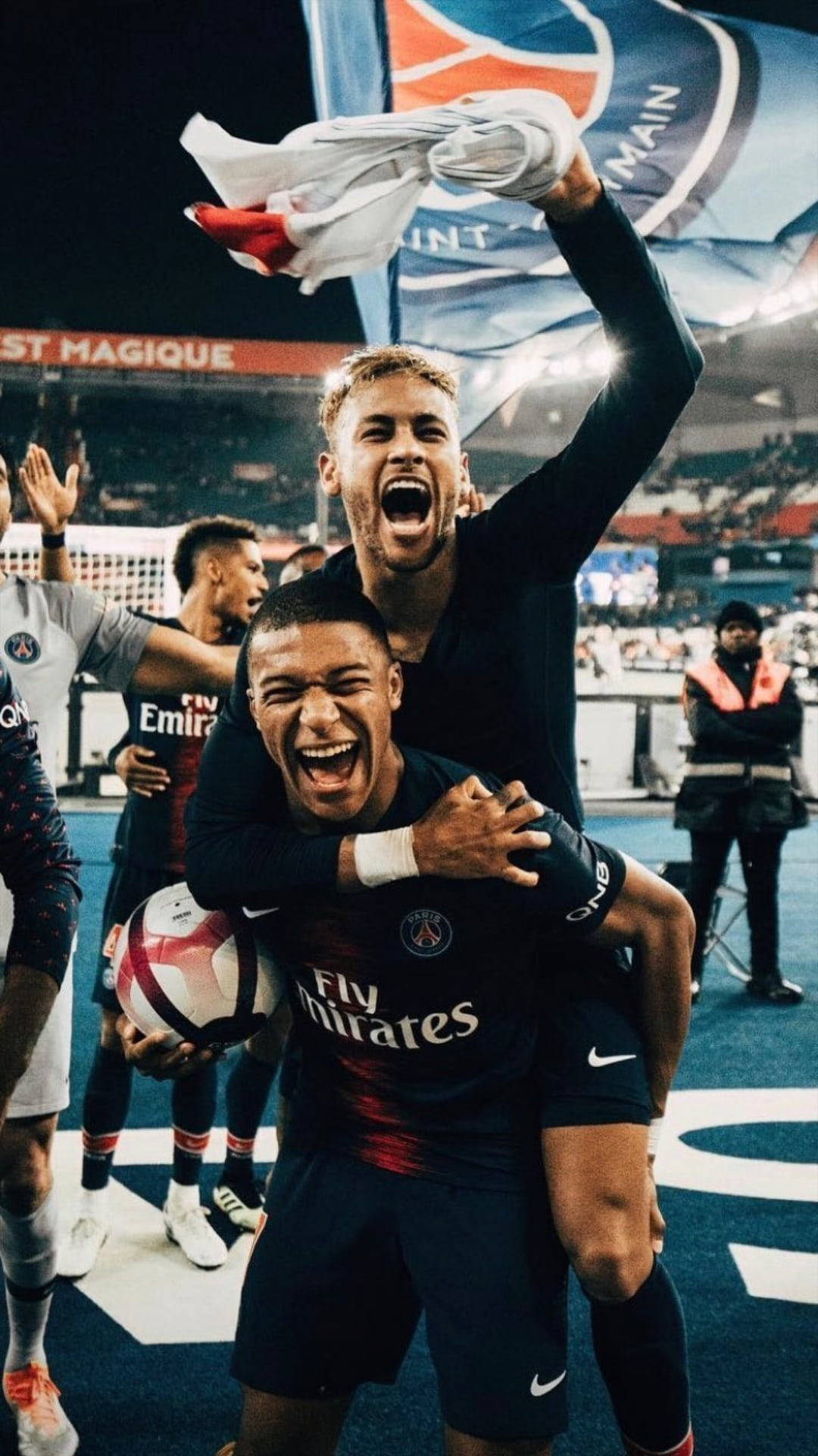 Kylian Mbappe 桌布 壁紙 — 兩名歡欣鼓舞的足球運動員在球場上慶祝勝利，一人高舉球衣，另一人抱著球。