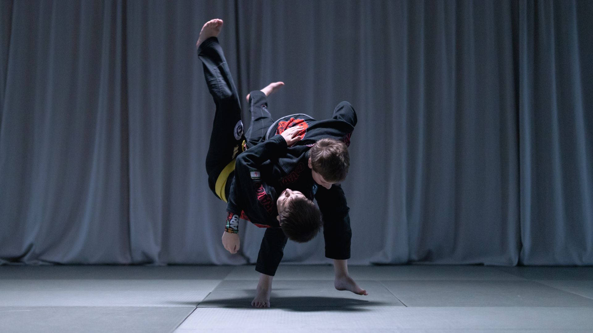 martial arts 桌布 壁紙 — 兩名武術家在灰色軟墊上進行動態纏鬥動作，背景為垂簾。