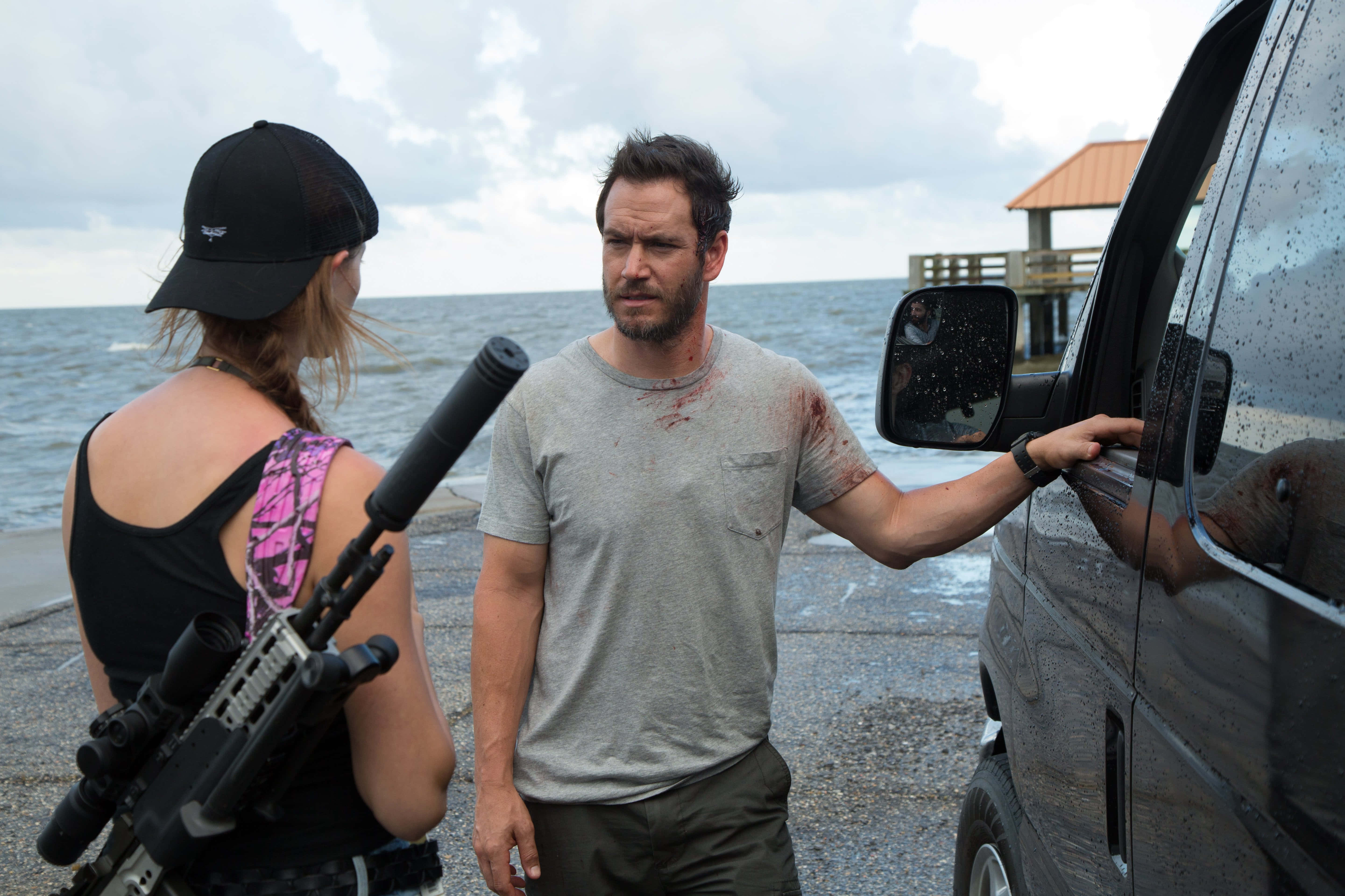 Mark-paul Gosselaar 桌布 壁紙 — 兩名武裝人士站在一輛廂型車旁，背景是暴風雨中的海灘和碼頭。