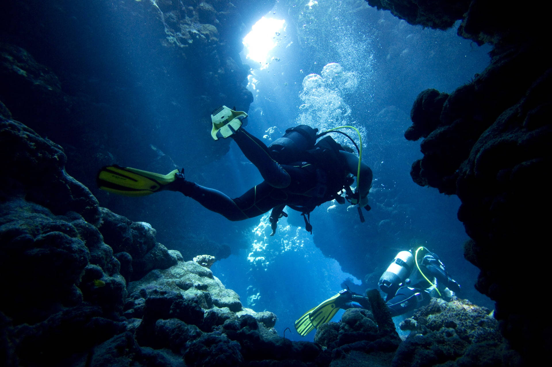 diving 桌布 壁紙 — 兩名水肺潛水員探索一個陽光照耀的水下洞穴，光束穿透藍色海水。