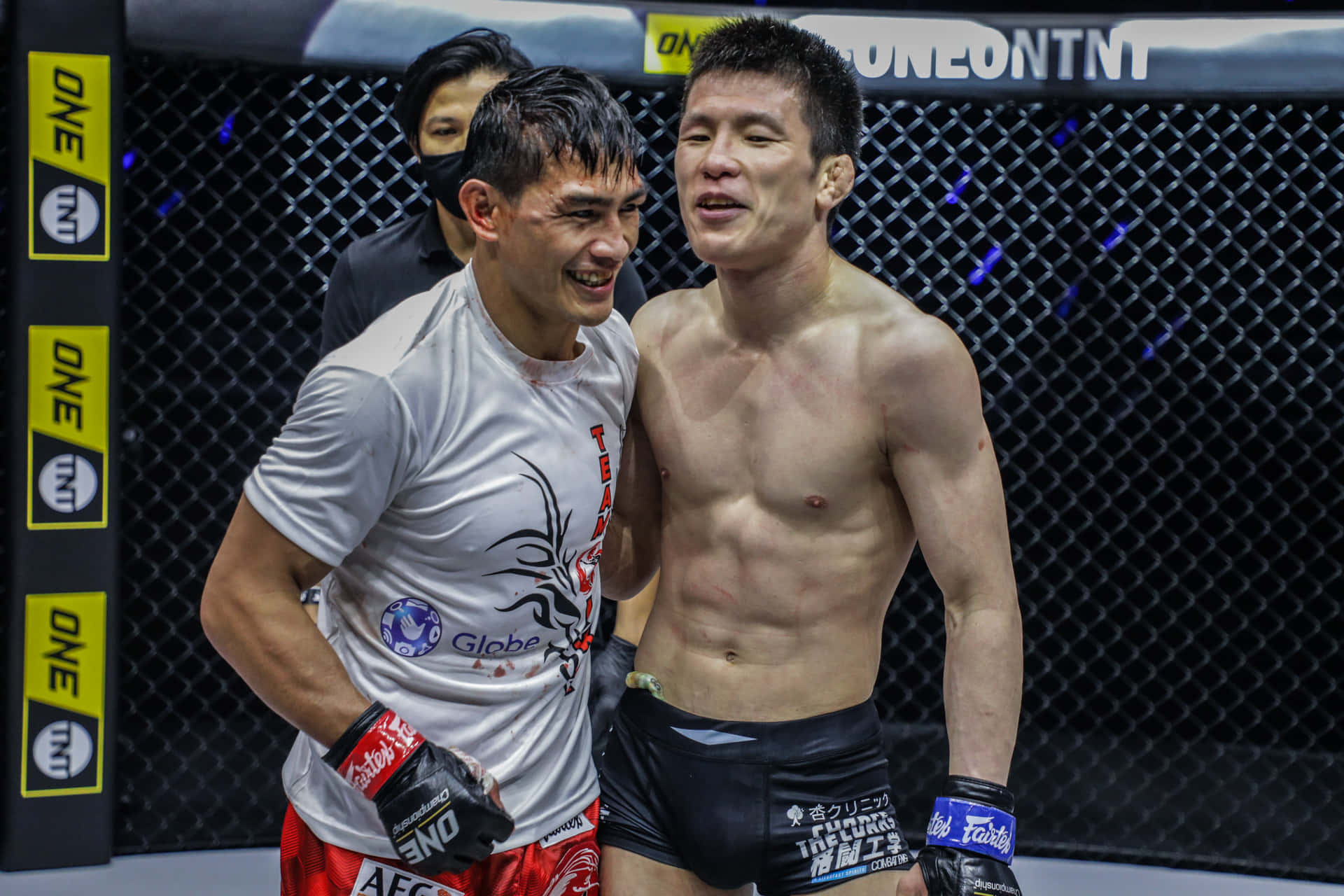 martial arts 桌布 壁紙 — 兩名汗流浹背的MMA拳手在籠中，於明亮的場館燈光下分享賽後時刻，展現笑容與友誼。