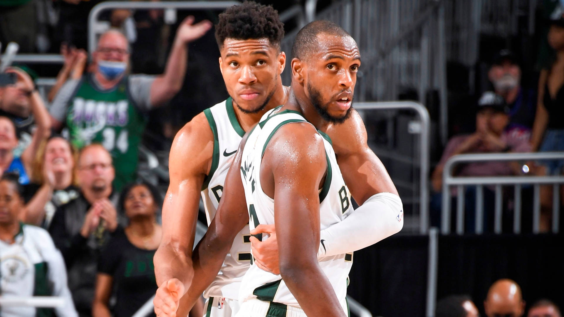 Khris Middleton 桌布 壁紙 — 兩名汗流浹背的籃球運動員身穿白色和綠色球衣，在比賽中專注，背景有歡呼的球迷。