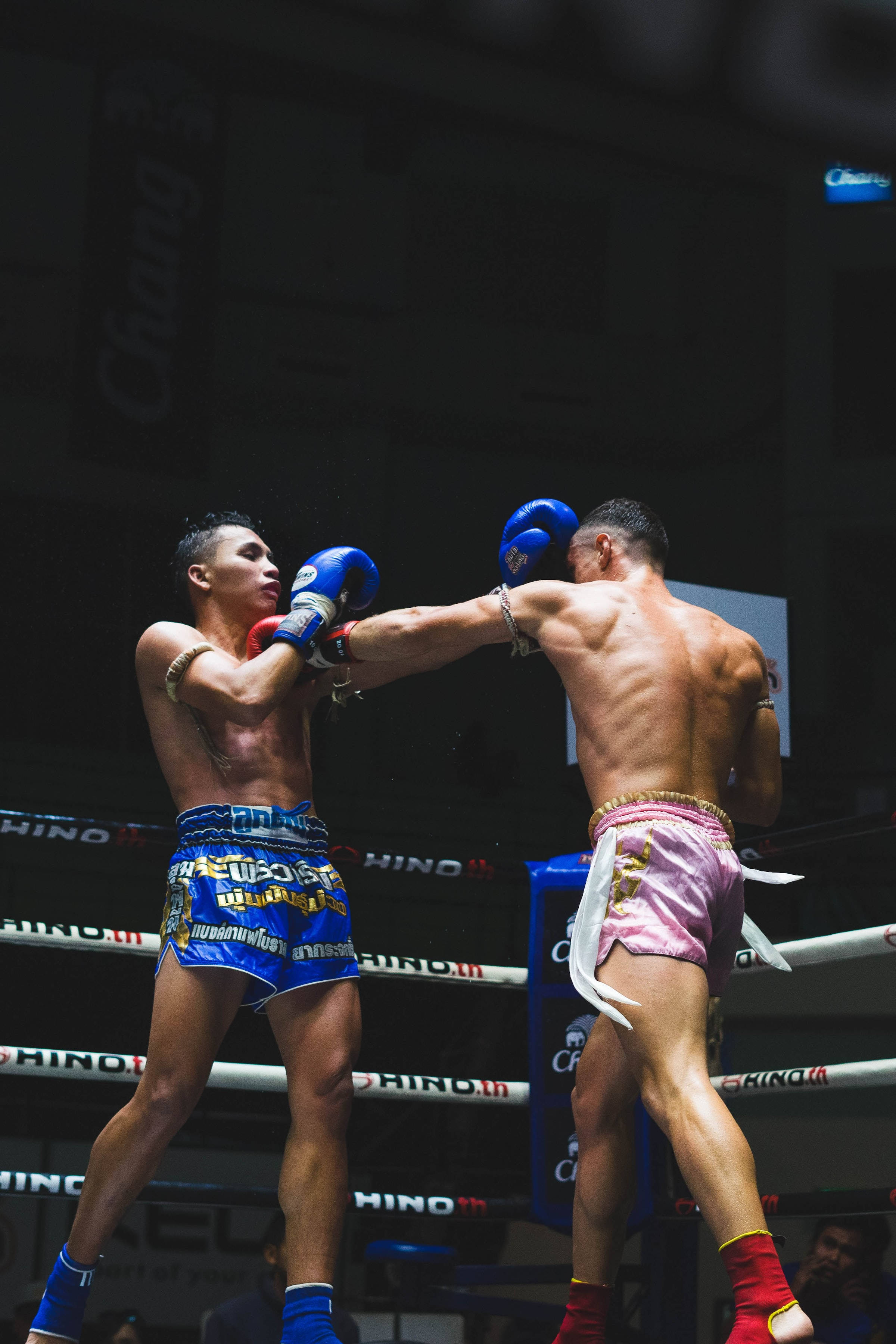 運動 桌布 壁紙 — 兩名泰拳拳手在燈光明亮的擂台上交鋒，一人出拳，另一人在戲劇性的燈光下格擋。