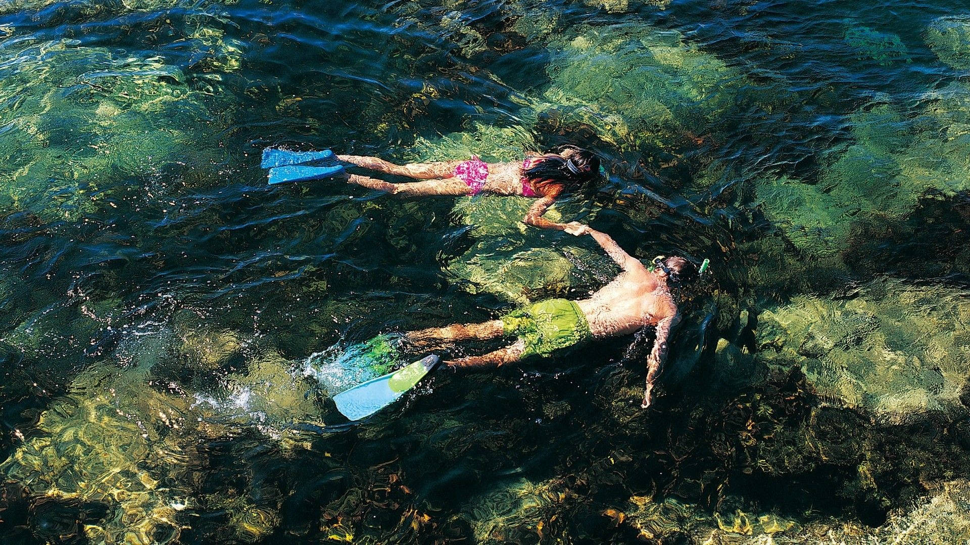 Snorkeling 桌布 壁紙 — 兩名浮潛者滑過清澈的碧綠海水，露出下方充滿活力的珊瑚和岩石。