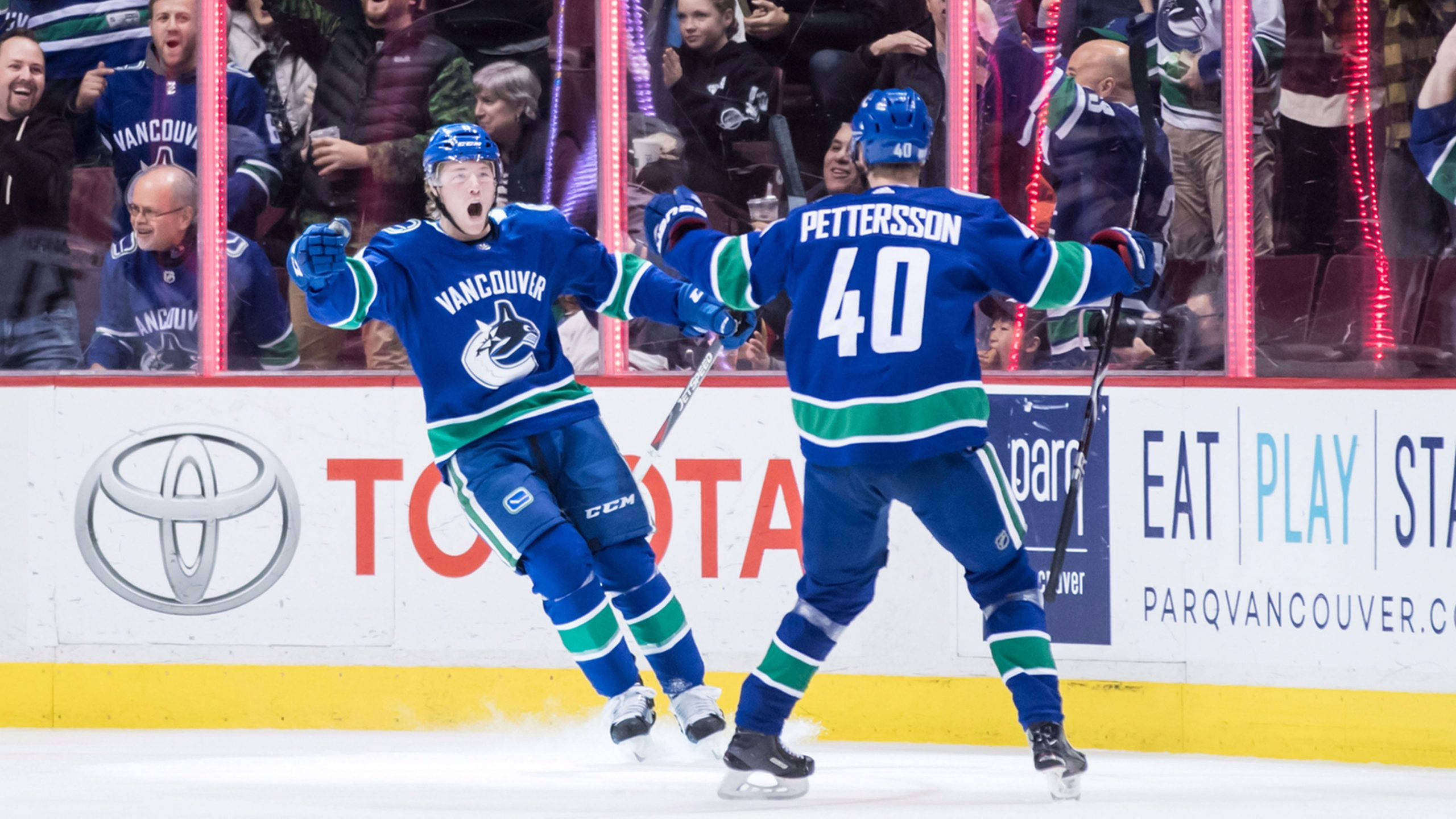 hockey 桌布 壁紙 — 兩名溫哥華加人隊（Vancouver Canucks）冰球球員在冰上慶祝進球，球迷在玻璃後歡呼。