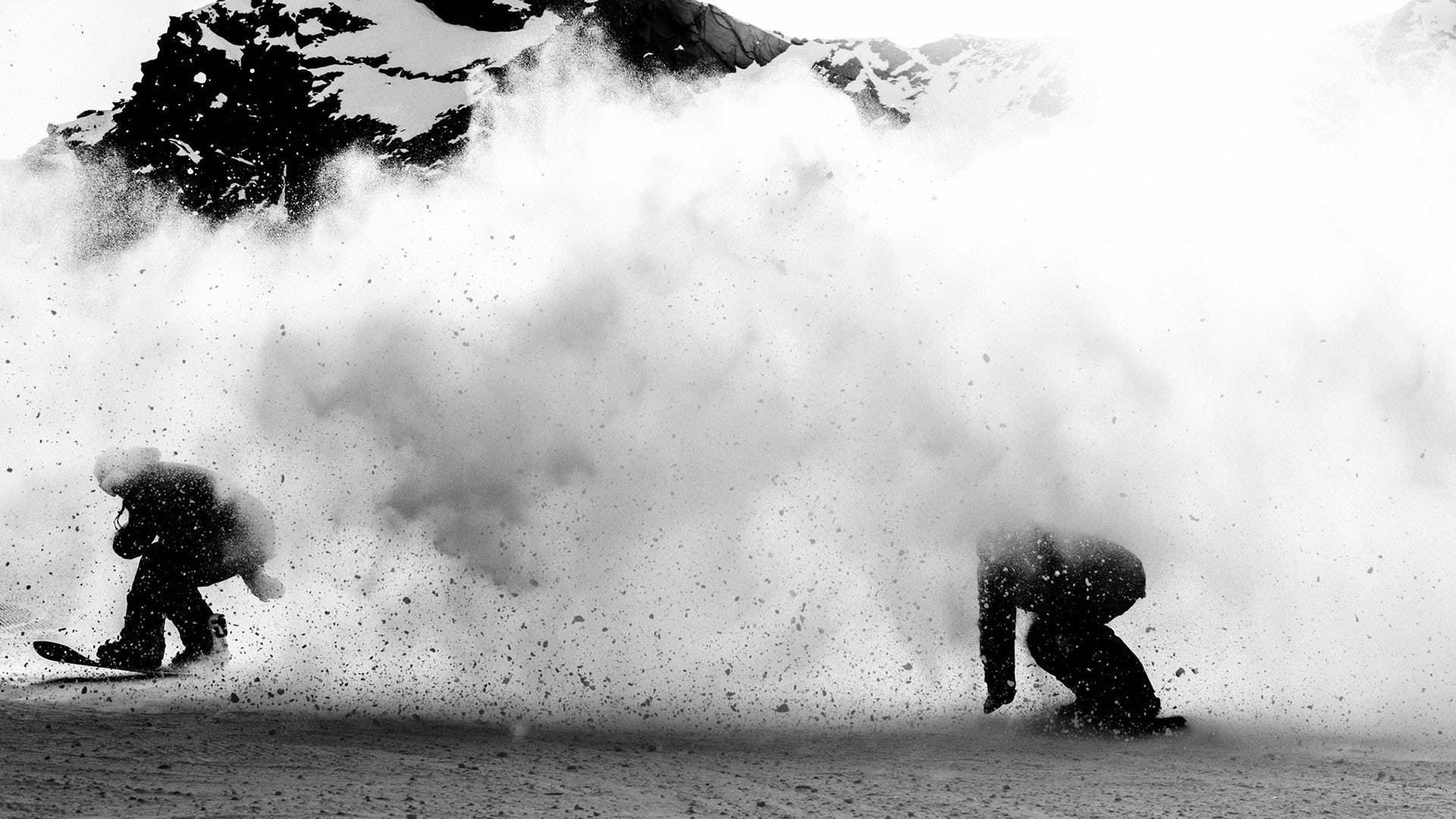 Snowboarding 桌布 壁紙 — 兩名滑雪板手在粉雪中轉彎，掀起大量雪花，背景是白雪皚皚的山脈。