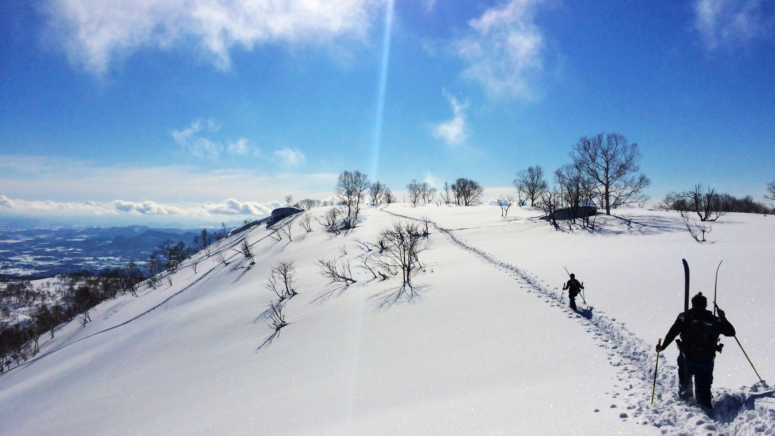 滑雪 桌布 壁紙 — 兩名滑雪者在明亮的藍天白雲下，沿著積雪的山脊向上跋涉。