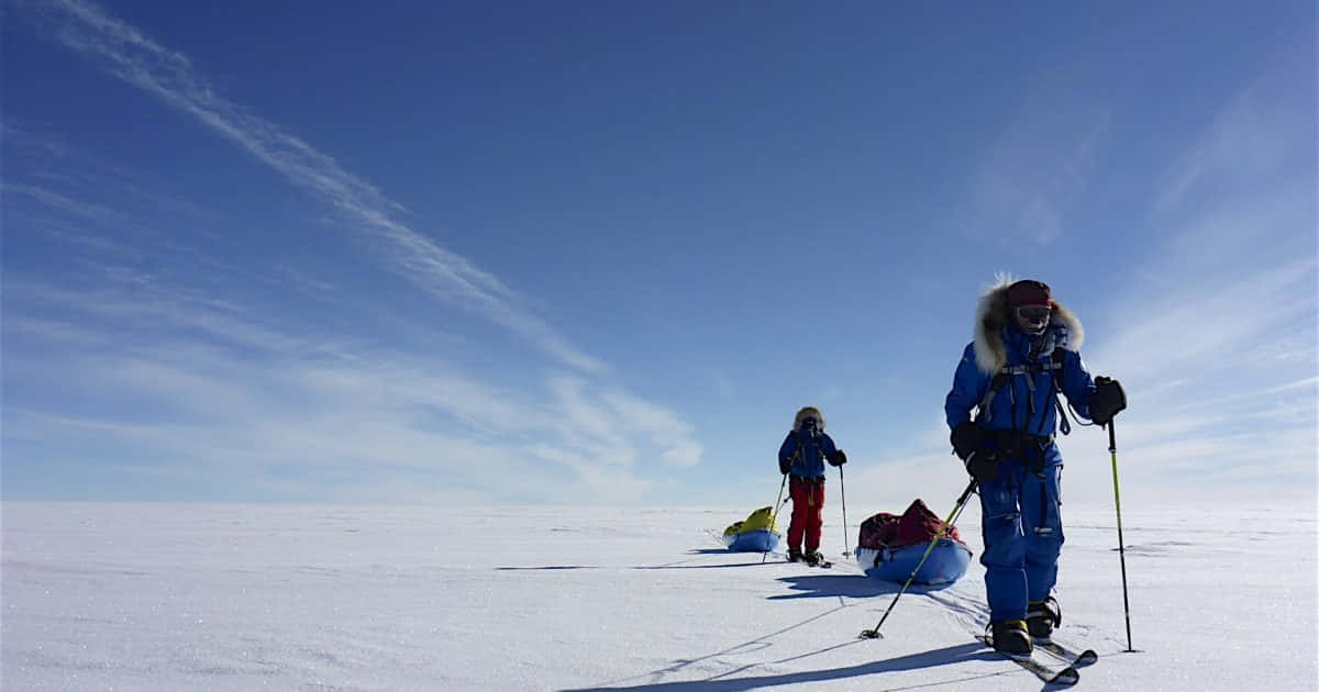 South Pole 桌布 壁紙 — 兩名滑雪者在晴朗藍天和薄雲下，穿越廣闊雪原。