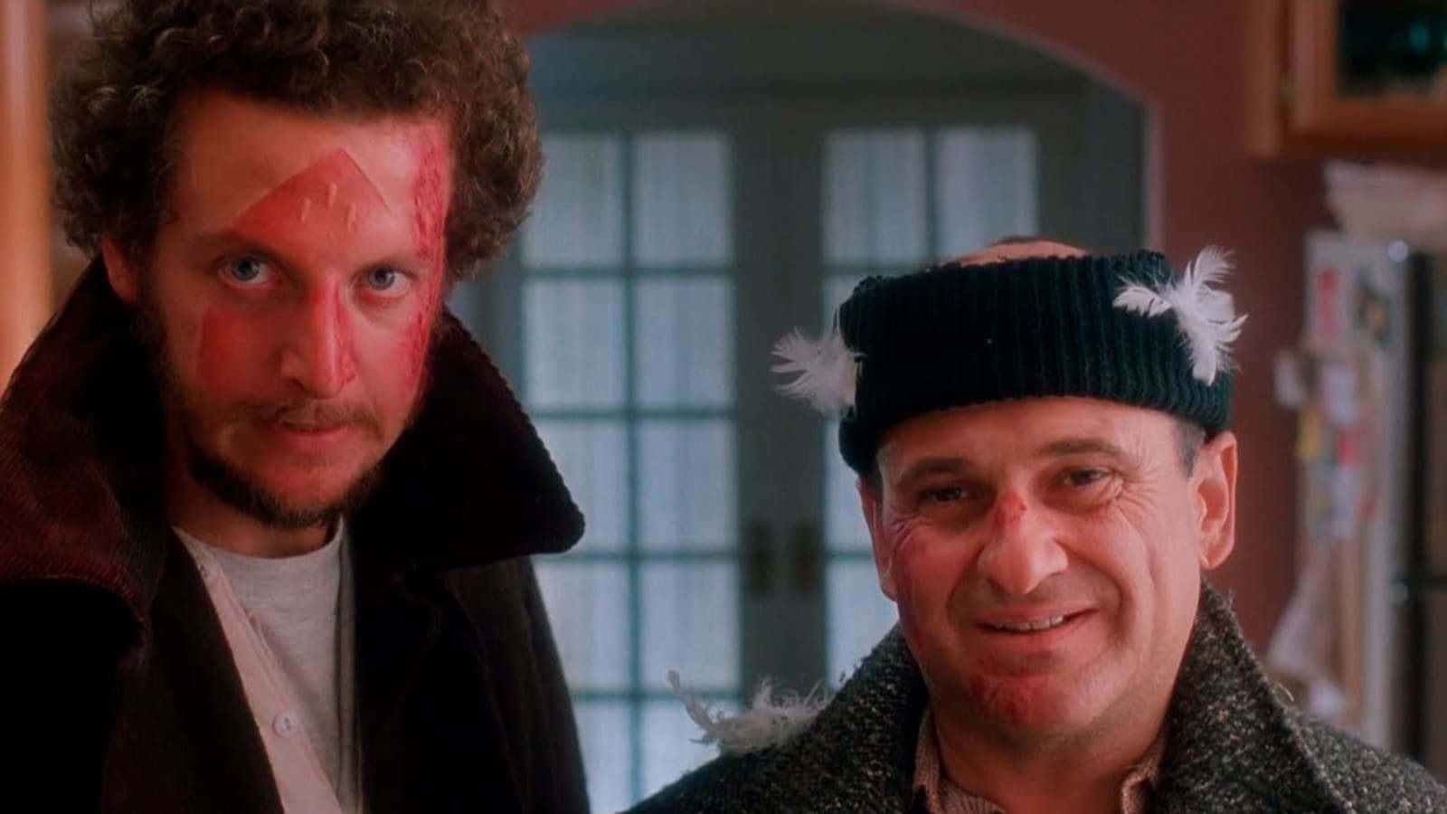 Home Alone Zoom 桌布 壁紙 — 兩名滿臉鮮血、戴著羽毛帽子的男子站在燈光溫暖的廚房門口。
