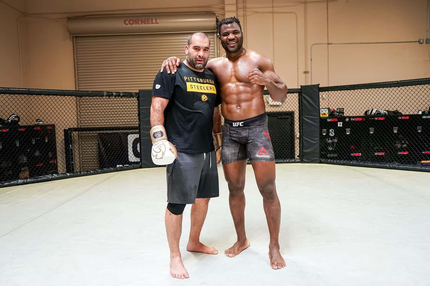 MMA 桌布 壁紙 — 兩名男子在UFC八角籠內自信地擺姿勢，一人赤裸上身展現肌肉線條，另一人穿著Steelers T恤，兩人都對著鏡頭微笑。