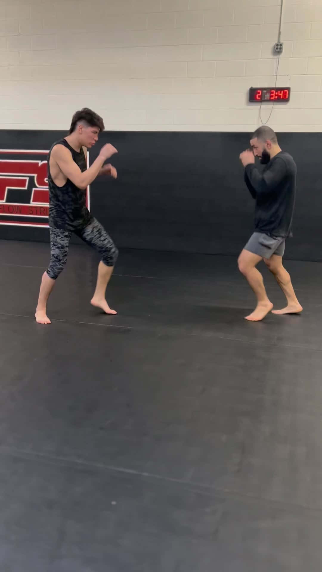 UFC 桌布 壁紙 — 兩名男子在健身房內對打，場地有黑色軟墊和一個顯示2:34:7的紅色數字時鐘。