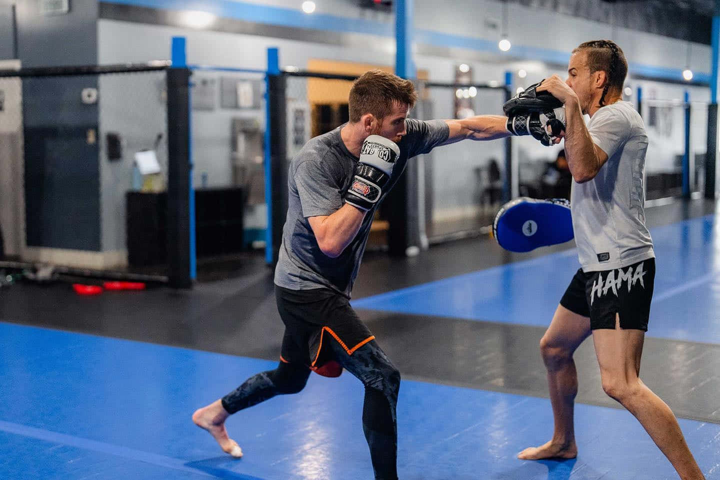 MMA 桌布 壁紙 — 兩名男子在健身房激烈訓練，一人出拳，另一人戴著手套在藍色墊子上阻擋。