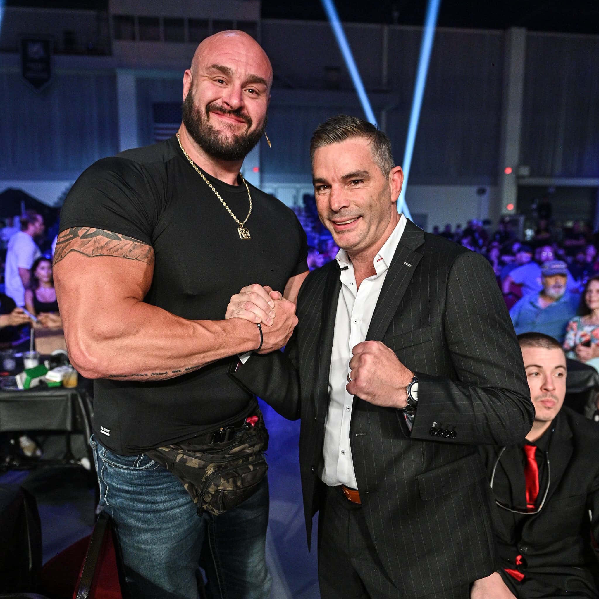 WWE 桌布 壁紙 — 兩名男子在熱鬧的室內活動中碰拳，背景有明亮的藍色舞台燈光和人群。