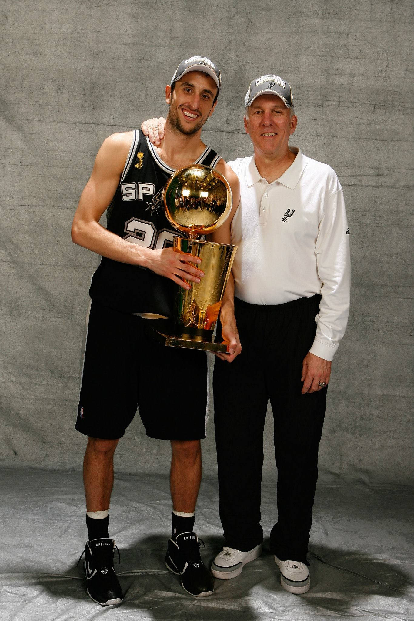 Manu 桌布 壁紙 — 兩名男子在純灰色背景前自豪地展示閃亮的NBA冠軍獎盃。