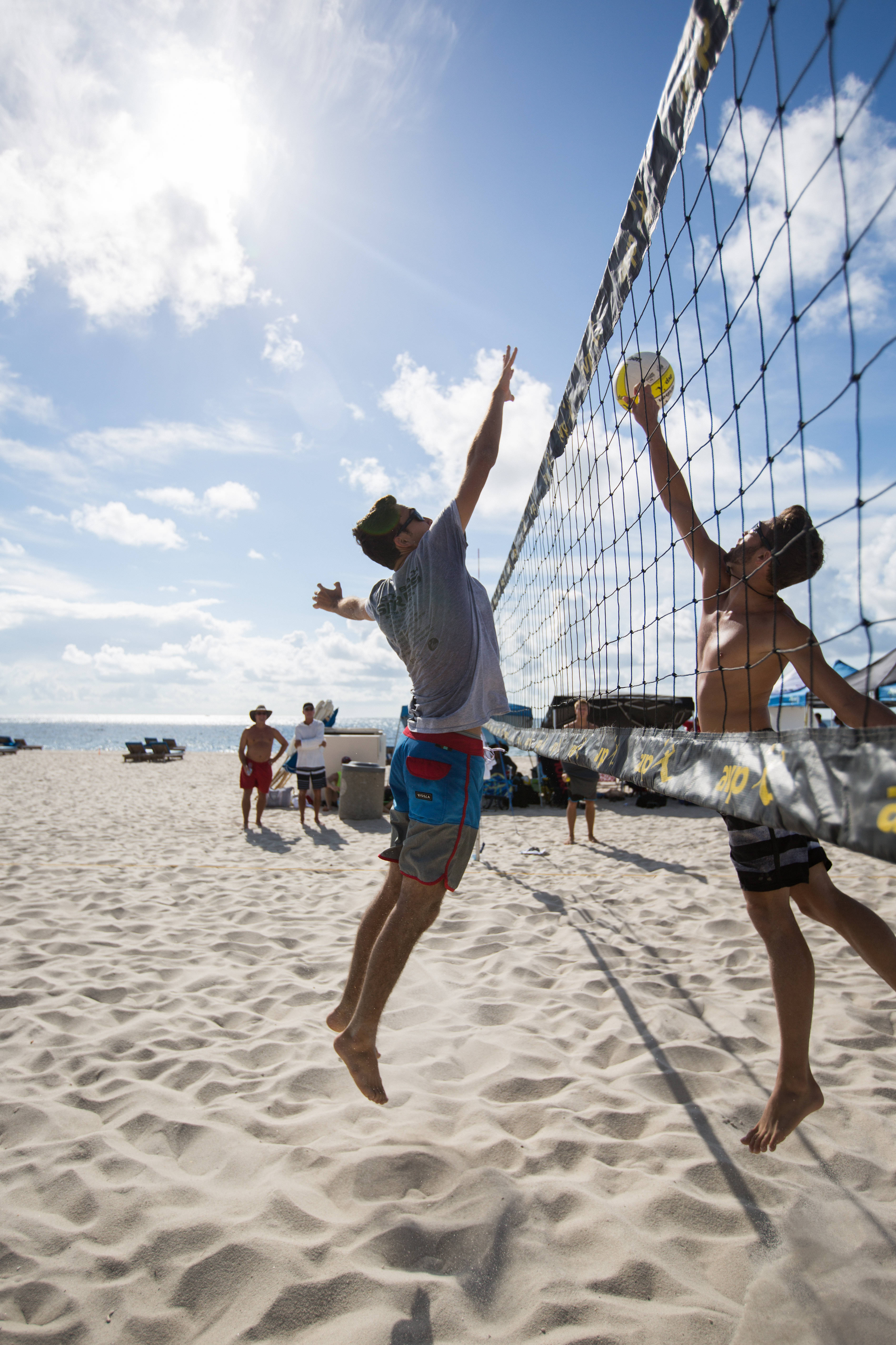 volleyball 4K 桌布 壁紙 — 兩名男子在陽光明媚的海灘上跳過排球網，背景是海洋和天空。
