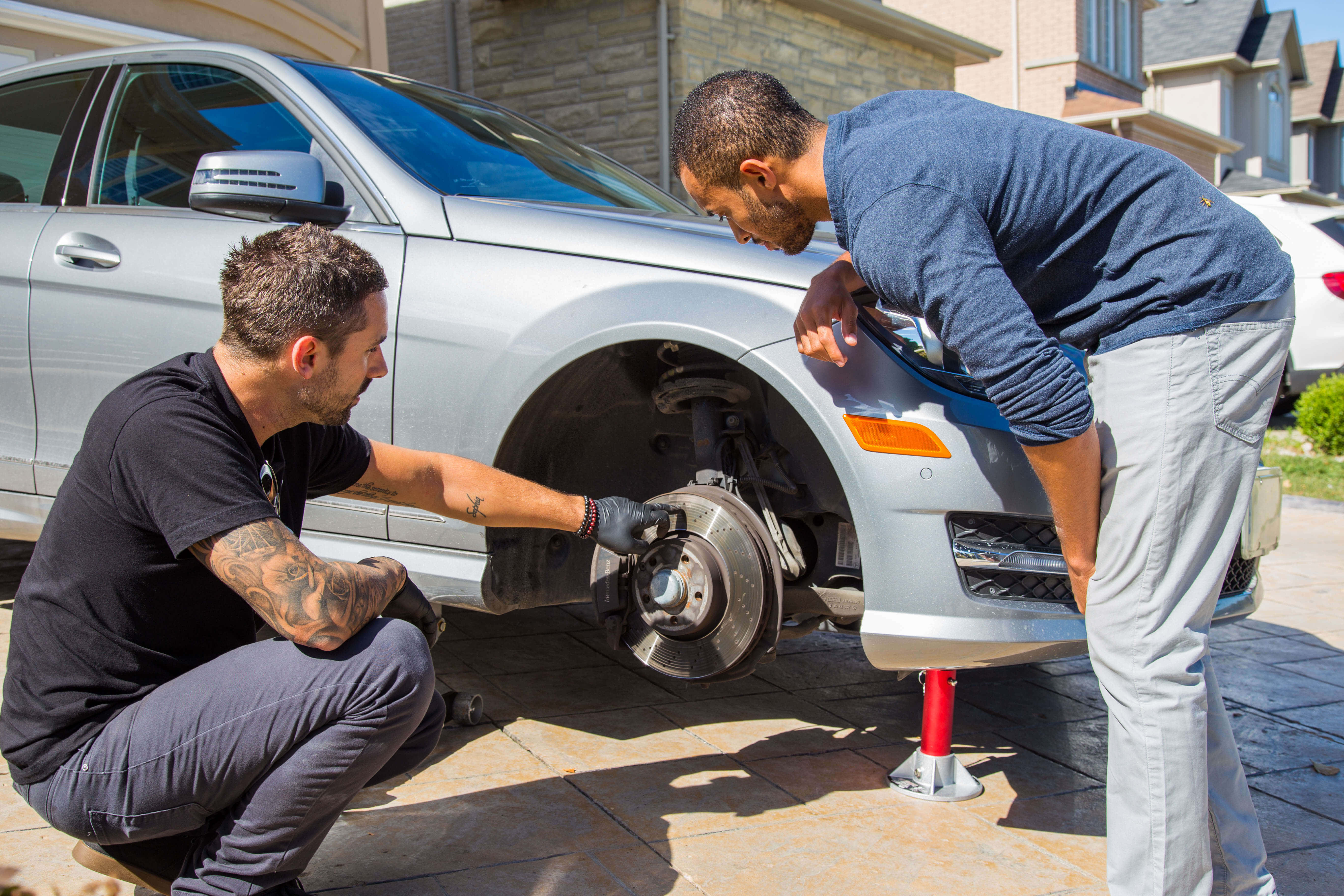 Car Repair 桌布 壁紙 — 兩名男子在陽光明媚的車道上用千斤頂修理銀色汽車的輪轂。