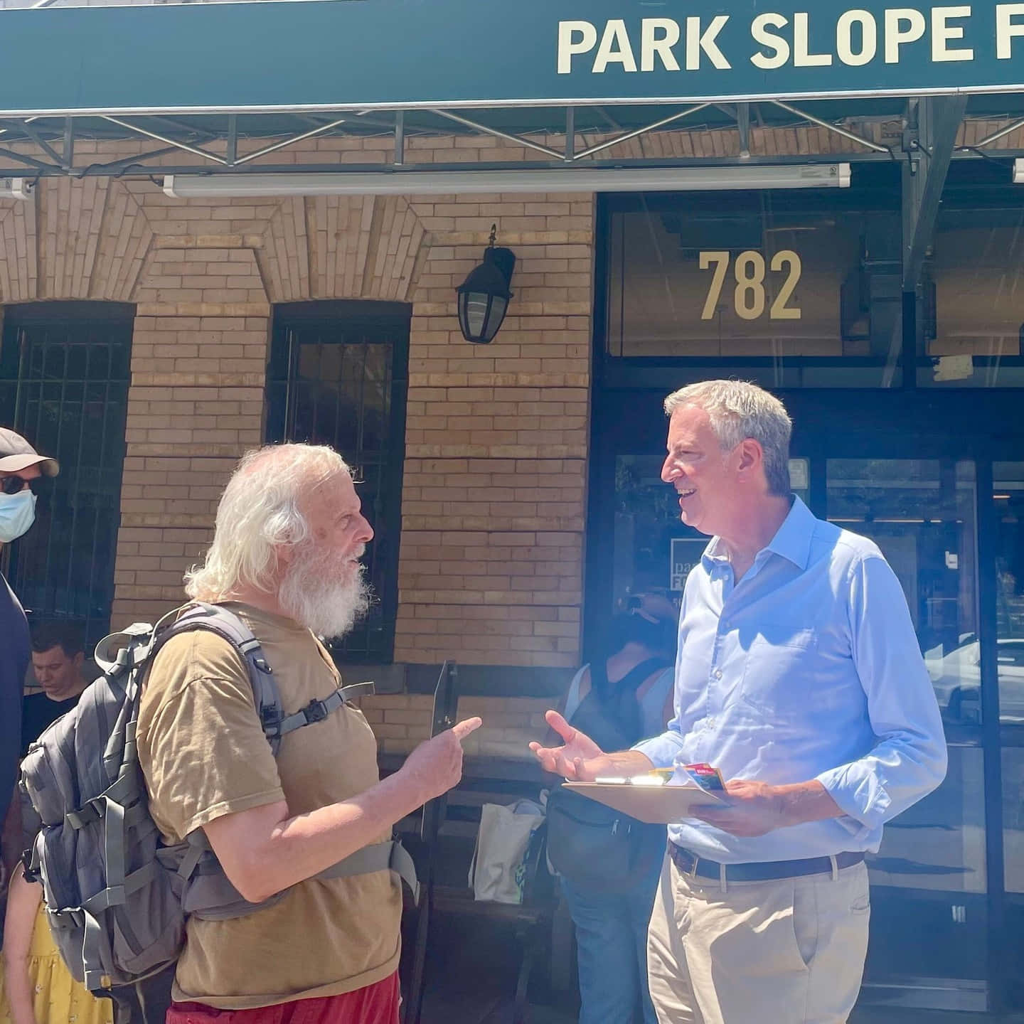 Talk 桌布 壁紙 — 兩名男子在陽光普照下，於一棟標有 Park Slope 782 的磚砌建築外熱烈交談。