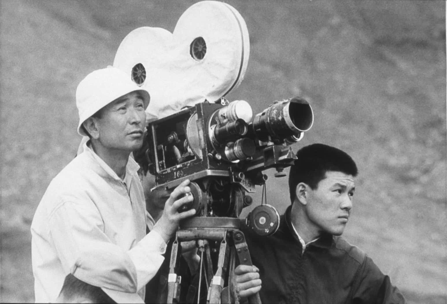 Akira Kurosawa 桌布 壁紙 — 兩名男子操作三腳架上的復古底片相機，背景是黑白模糊的岩石。
