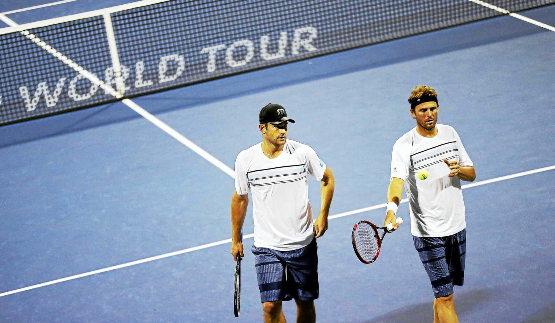 Tennis 桌布 壁紙 — 兩名男子網球選手在世界巡迴賽比賽期間，在明亮的體育場燈光下走過藍色硬地球場。