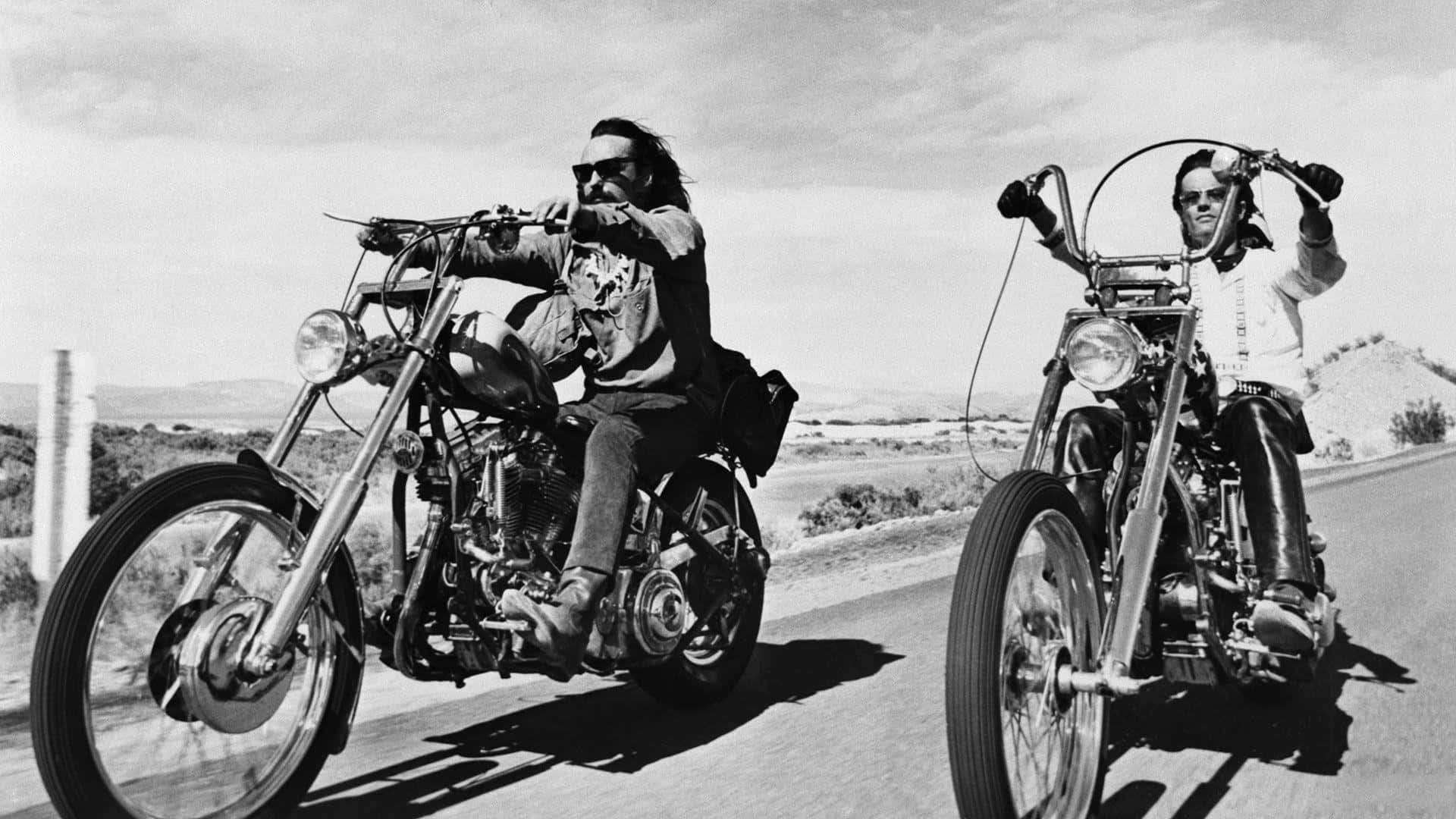 biker 桌布 壁紙 — 兩名男子騎著定制chopper摩托車，在陽光明媚的沙漠公路上行駛，背景是崎嶇的地形。