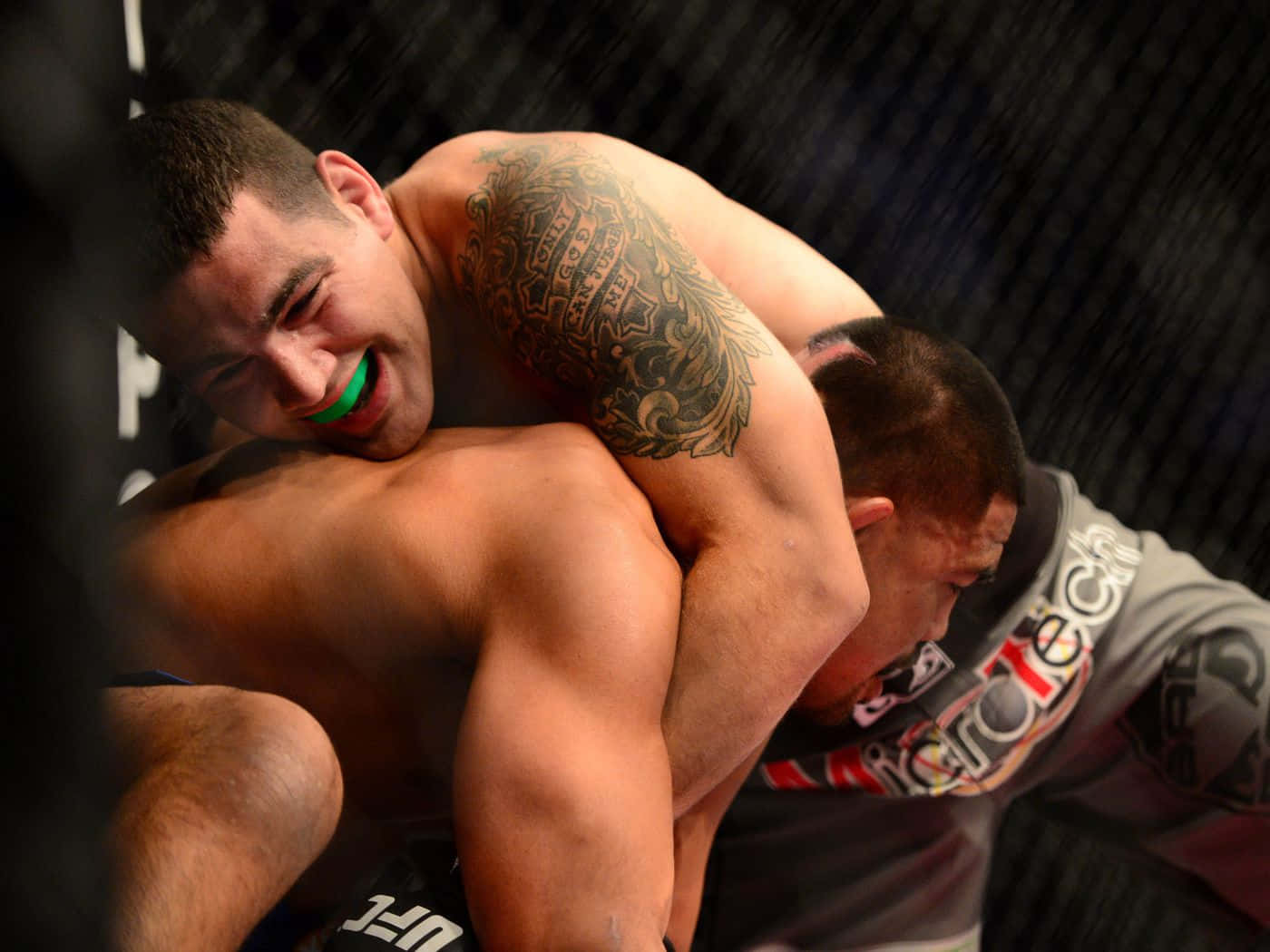MMA 桌布 壁紙 — 兩名男性拳手在UFC八角籠中激烈纏鬥，其中一人面露痛苦表情，同時施展鎖喉技。