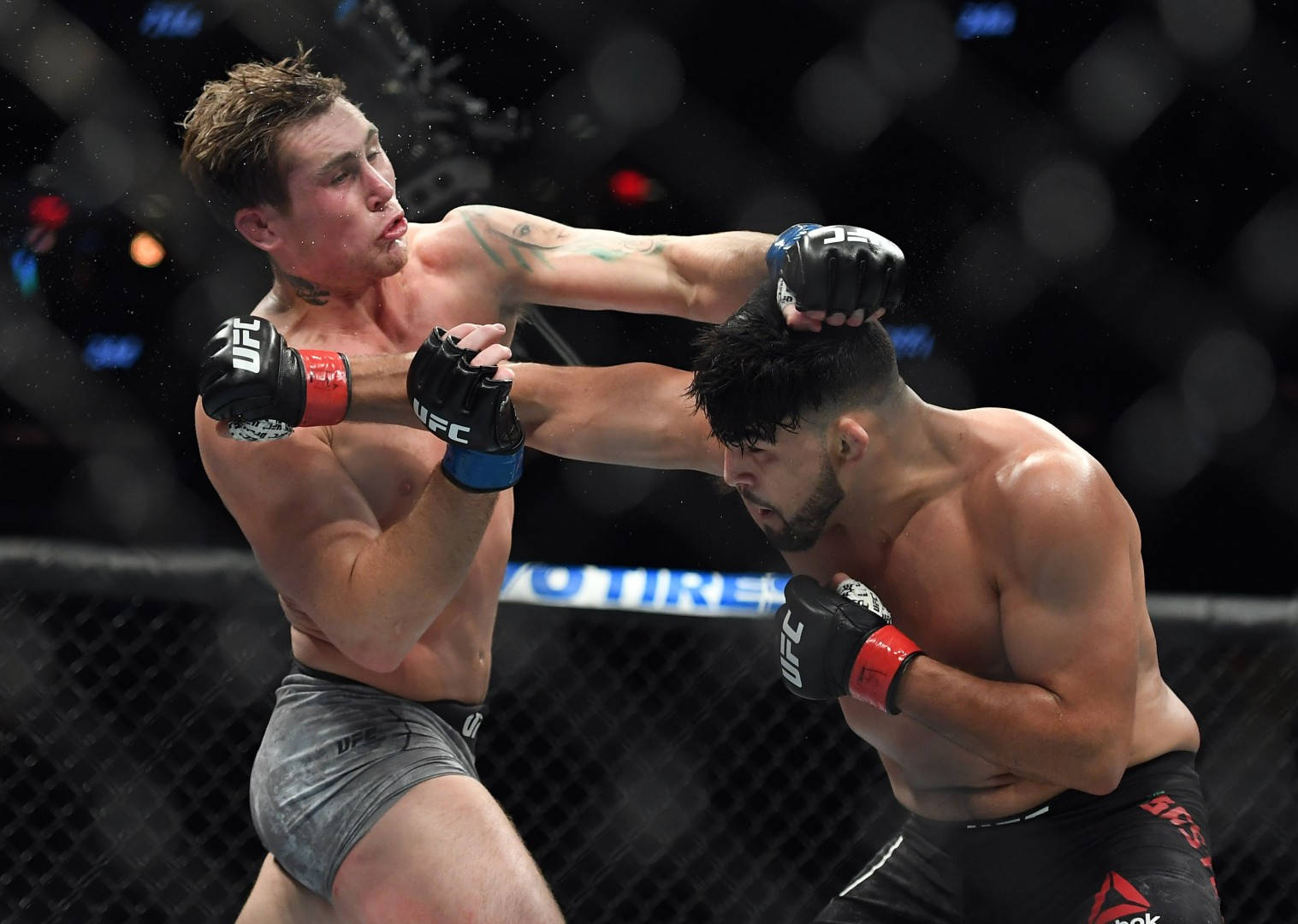 UFC 桌布 壁紙 — 兩名男性拳手在激烈的UFC比賽中交鋒，汗水飛濺，其中一人在八角籠內打出強力一拳。