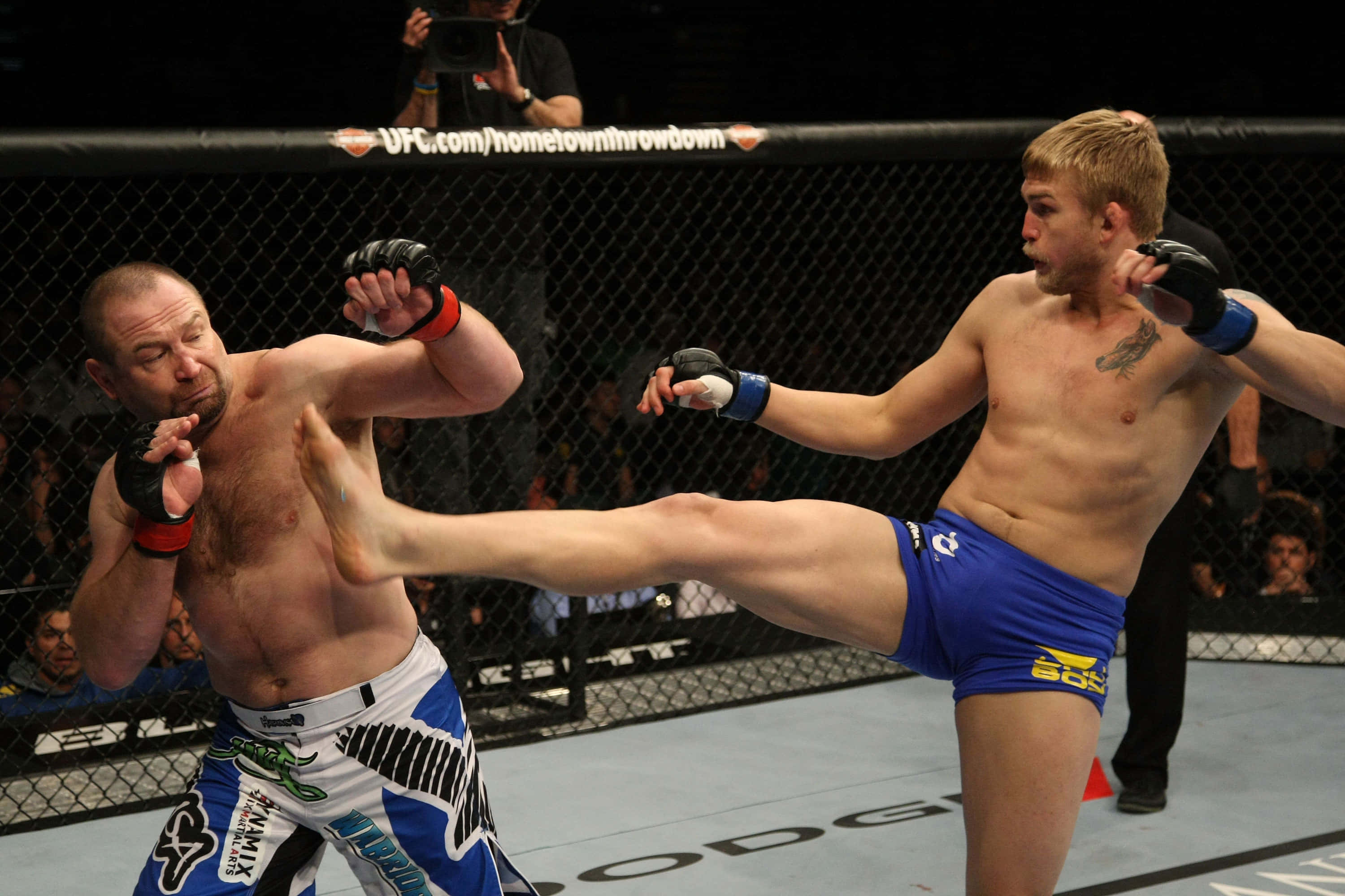 UFC 桌布 壁紙 — 兩名男性拳手在籠中，一名使出高踢，另一名在UFC比賽中阻擋。