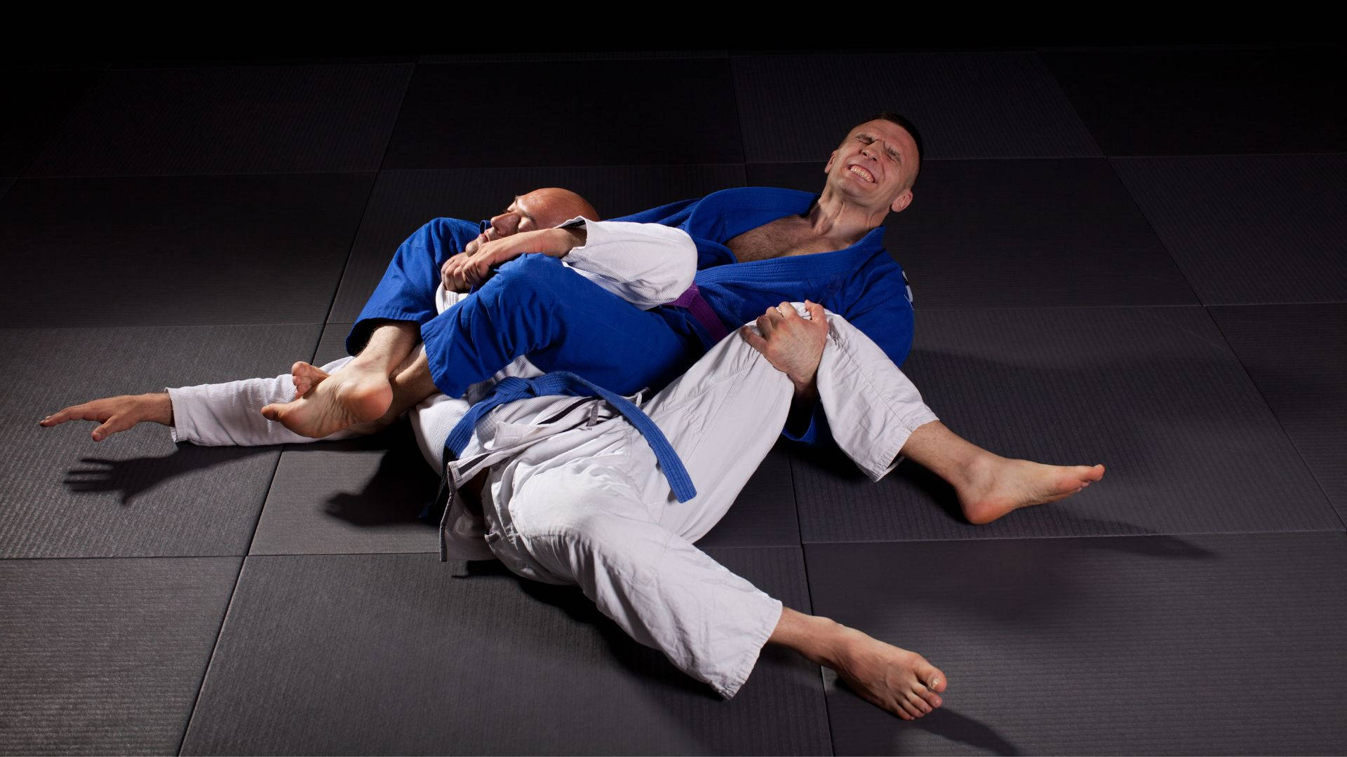 martial arts 桌布 壁紙 — 兩名男性柔道選手在戲劇性的工作室燈光下，於深色墊子上激烈纏鬥。