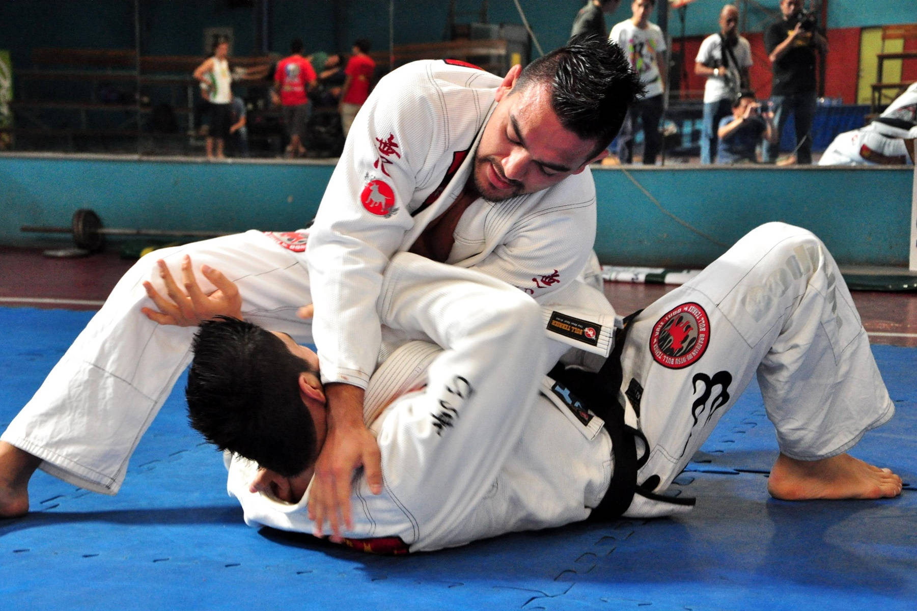martial arts 桌布 壁紙 — 兩名男性柔道選手在藍色墊子上激烈纏鬥，背景有觀眾觀看比賽。