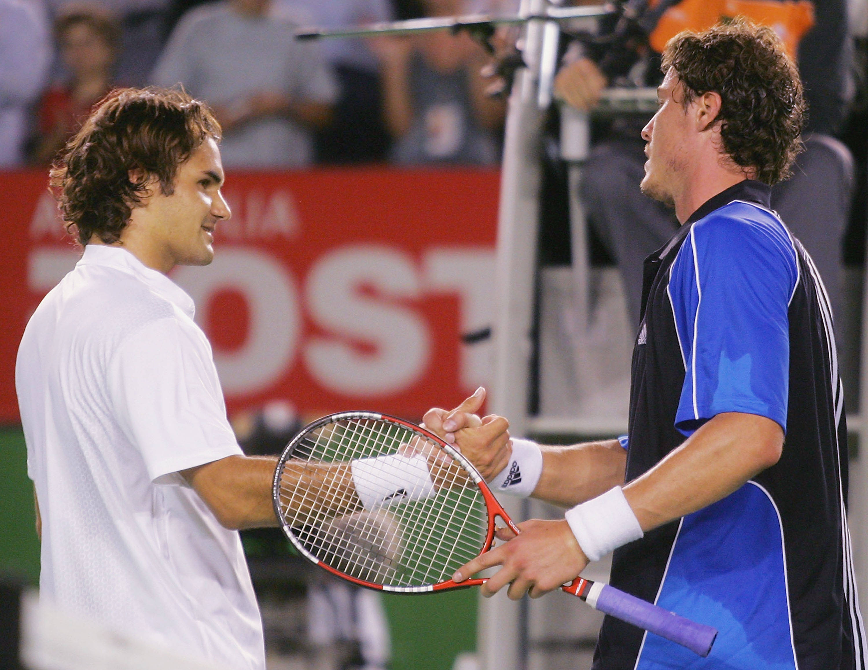 Australian Open 桌布 壁紙 — 兩名男性網球運動員在球場上握手，其中一人手持球拍，身後有紅色贊助商橫幅。