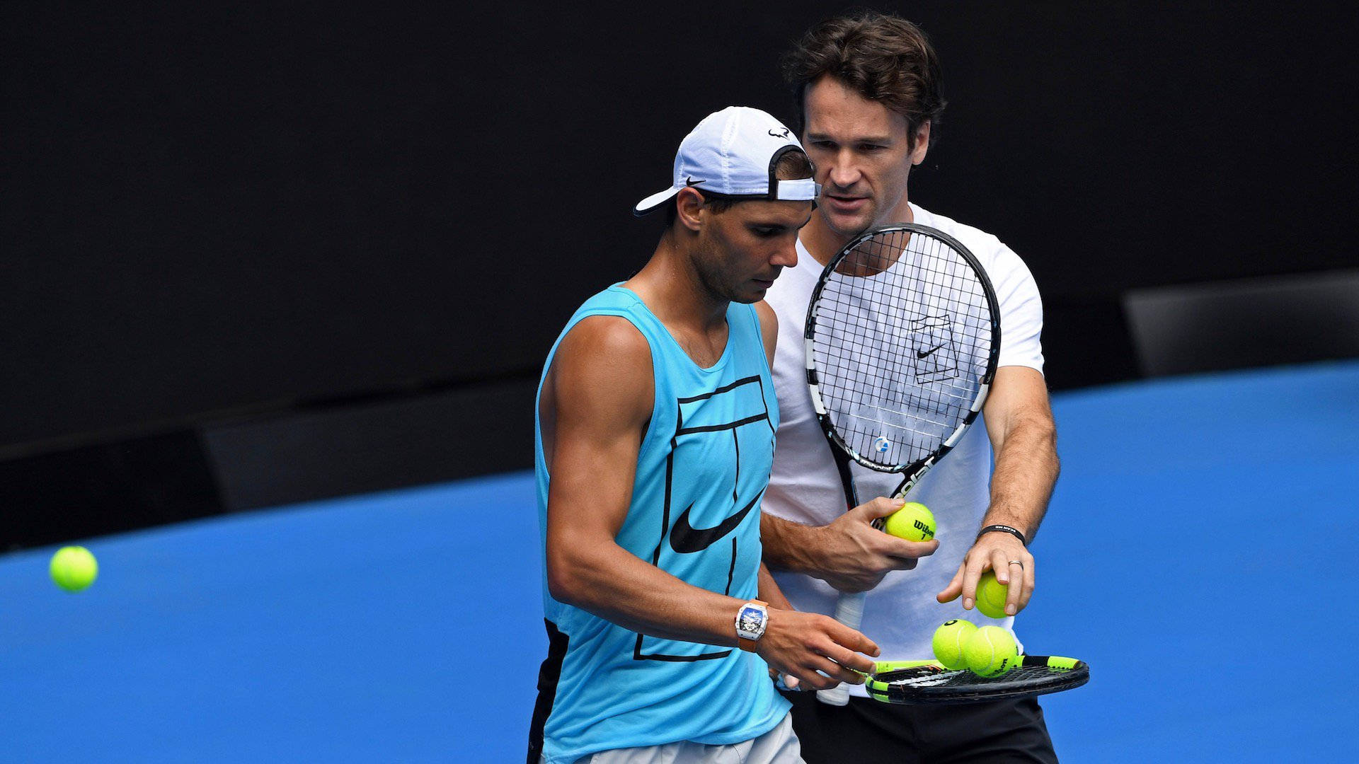 Tennis 桌布 壁紙 — 兩名男性網球運動員在藍色球場上比賽，一人穿藍色背心，另一人穿白色襯衫，手持球拍和網球。
