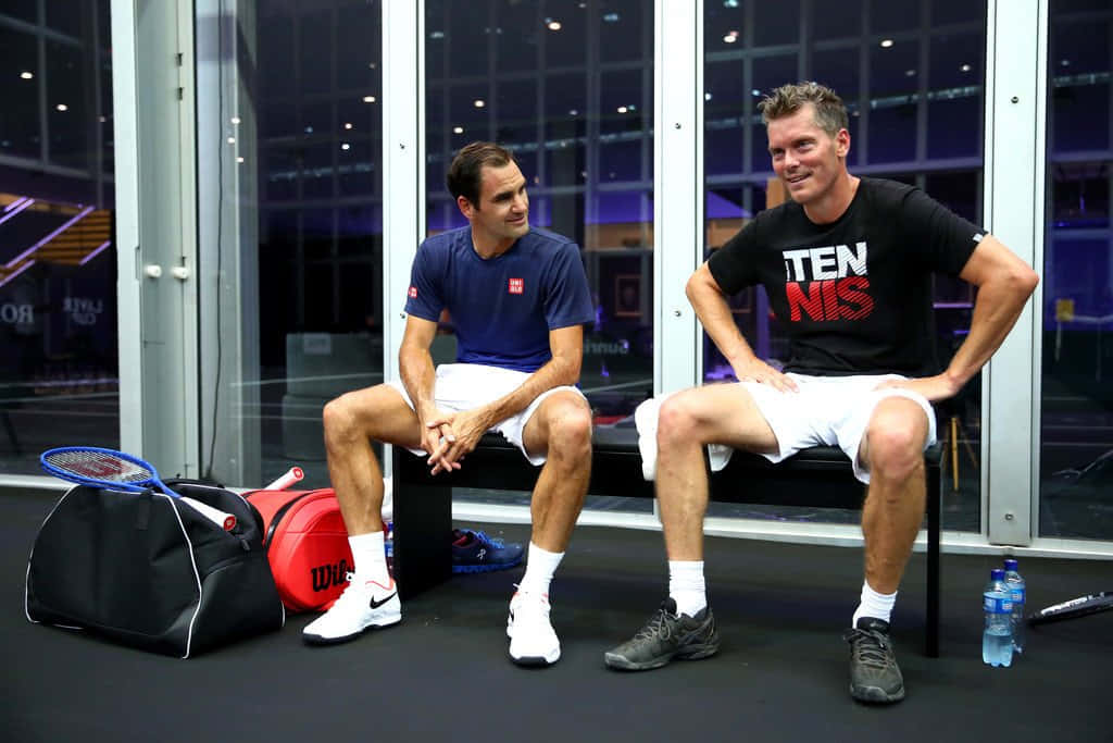 Tennis 桌布 壁紙 — 兩名男性網球運動員放鬆地坐在長椅上，旁邊放著裝備，背後玻璃門透出城市燈光。