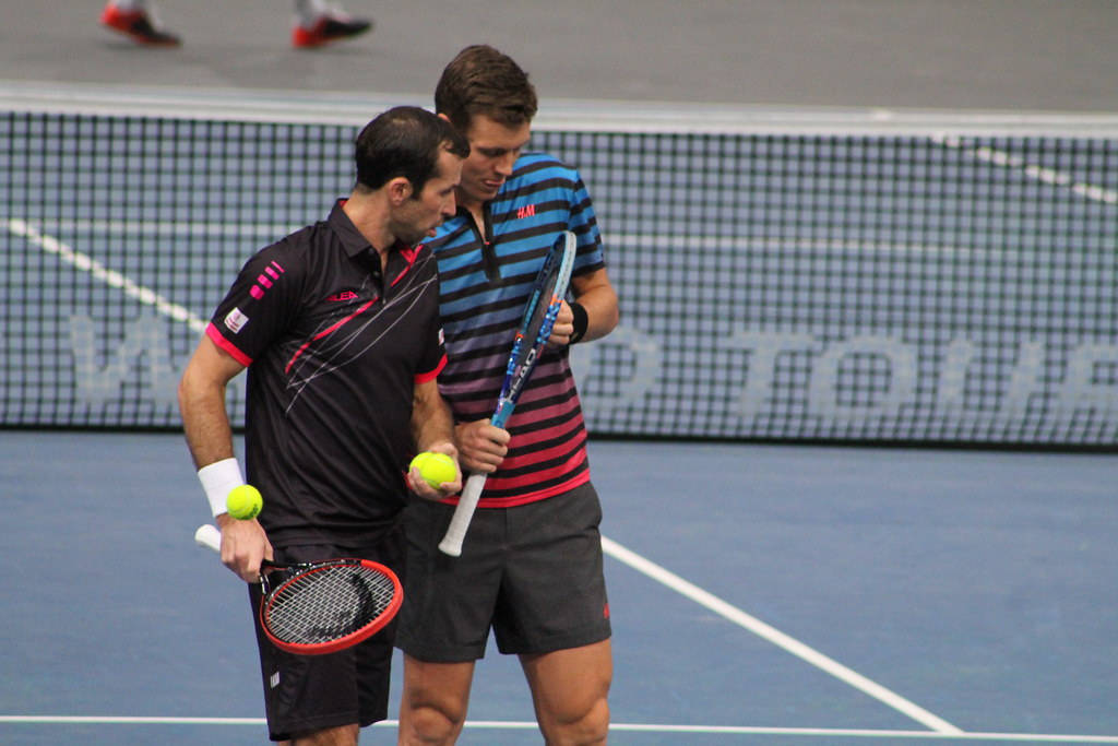 Tennis 桌布 壁紙 — 兩名男性網球運動員穿著運動裝備，在藍色球場上拿著球拍和球進行比賽。