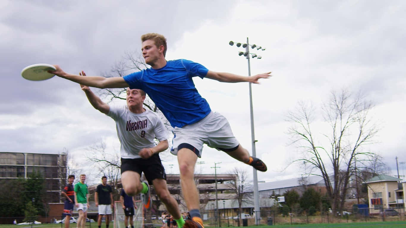 1366x768 Ultimate Frisbee 桌布 壁紙 — 兩名男性運動員在陰天戶外場地動態躍起，爭奪飛行的飛盤。