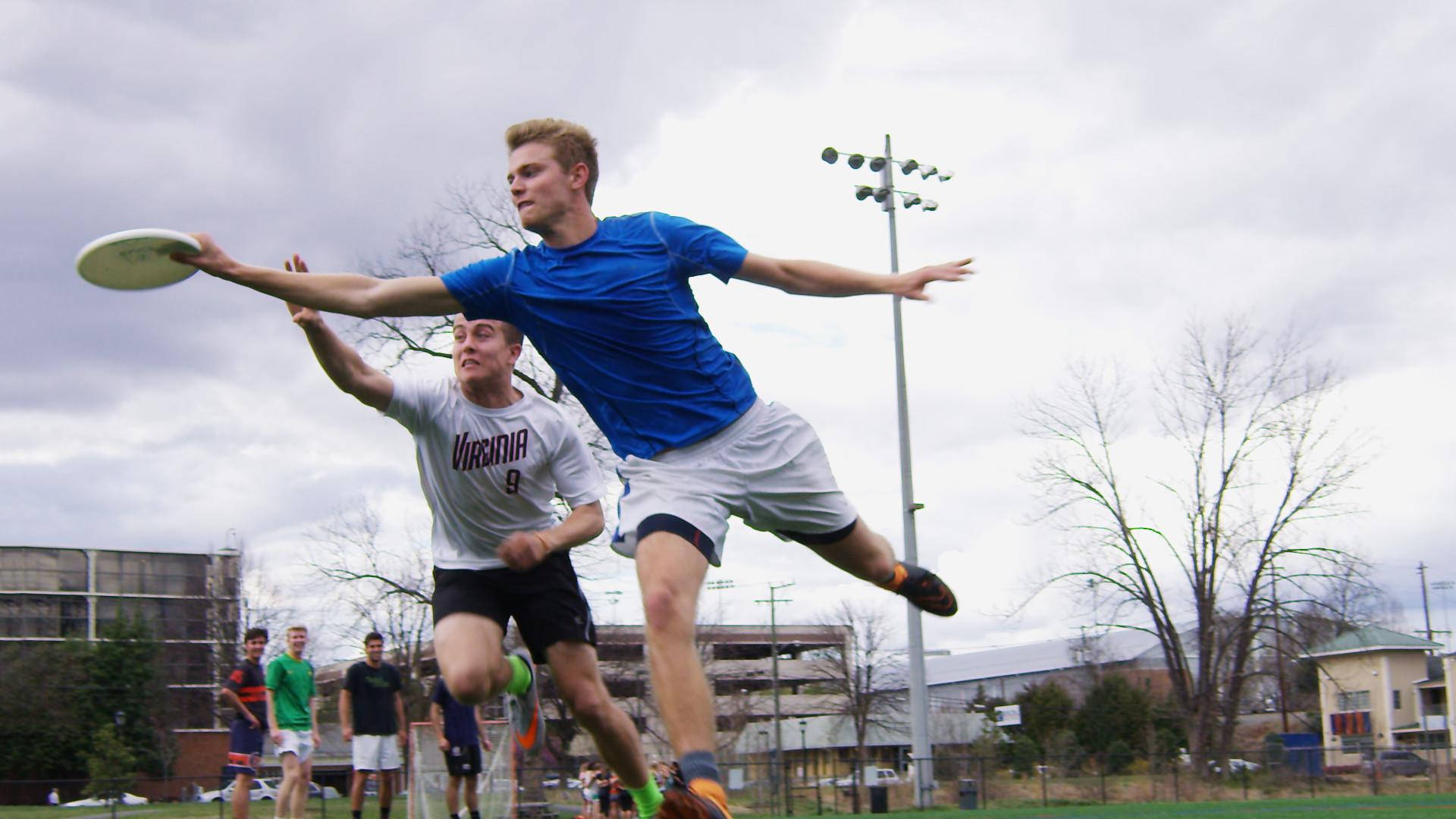 Ultimate Frisbee 桌布 壁紙 — 兩名男性運動員在陰天戶外運動場上動態地躍起爭奪飛行的飛盤。